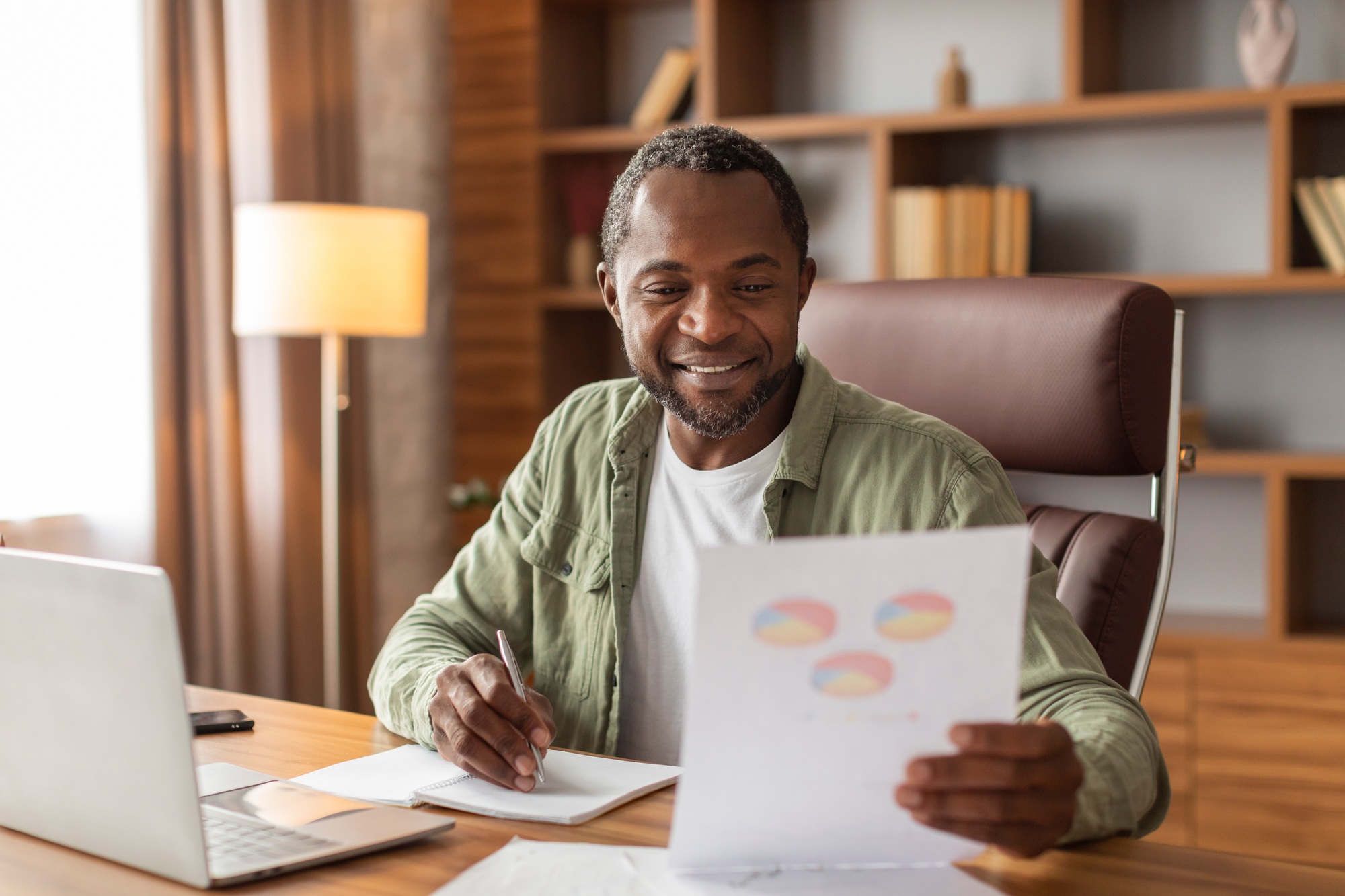 Cheerful busy middle aged black guy makes notes and works with graphs and charts, analysis financial