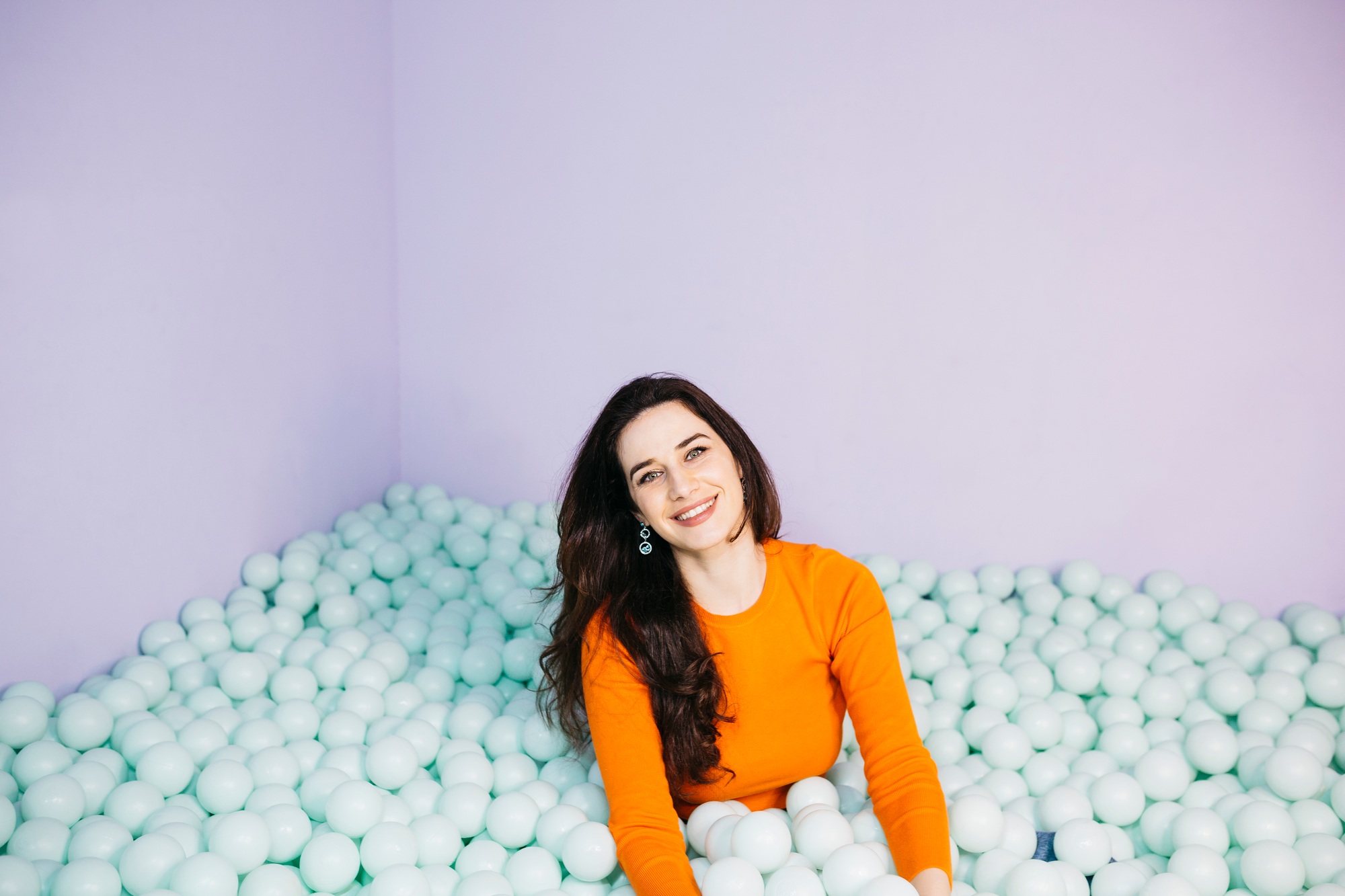 Cheerful influencer posing in a ball pit filled with pastel balls for social media content creation