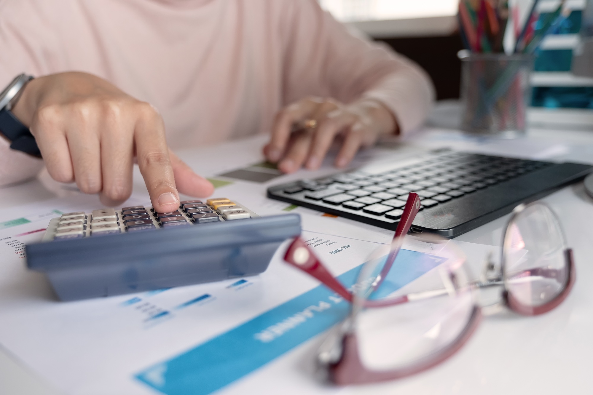 Close up Businessman hand holding pen and pointing at finance paperwork and using calculator for do