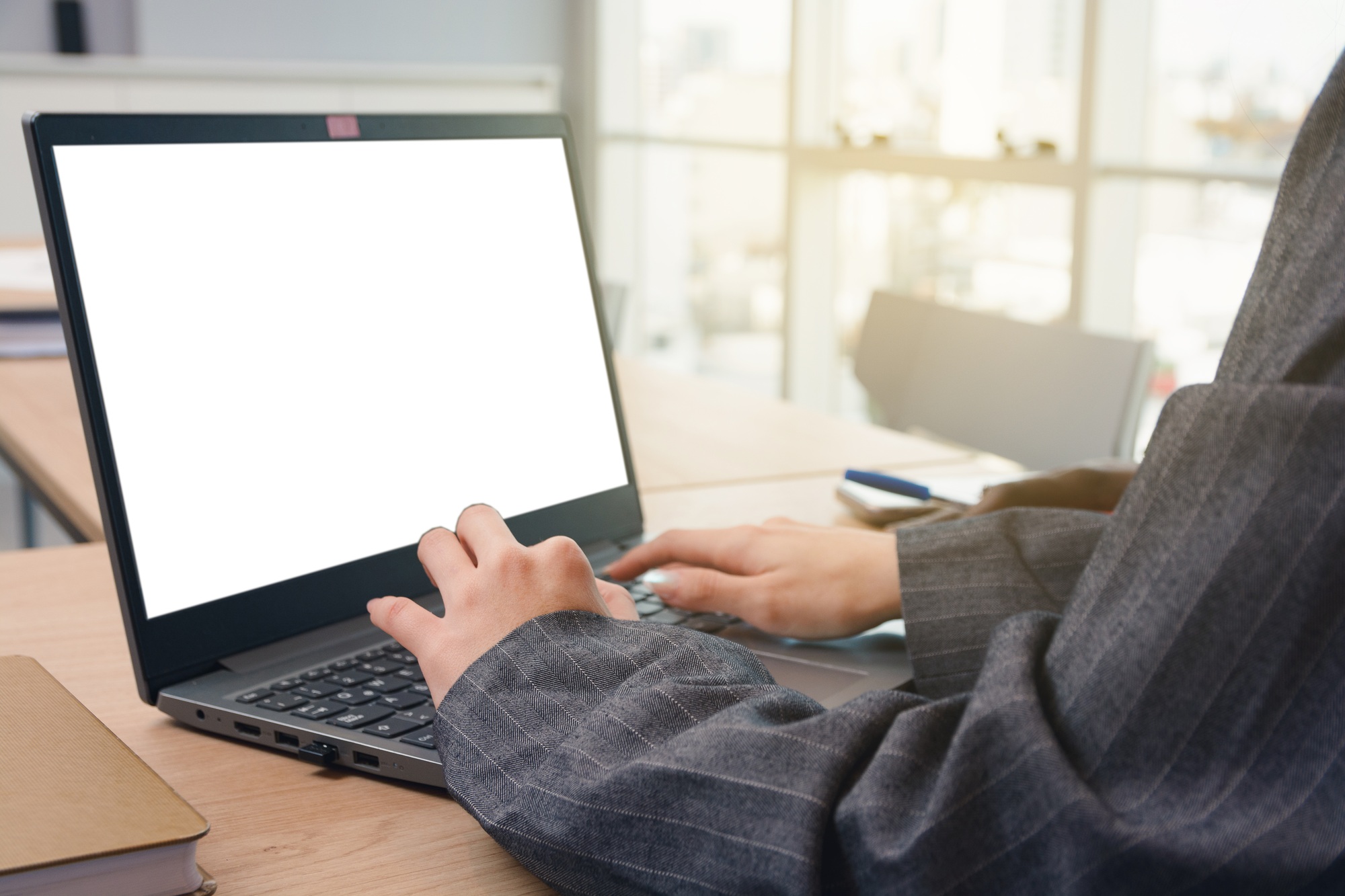 Close up of a unrecognizable Woman typing on a laptop with a blank screen on the desk, copy space.