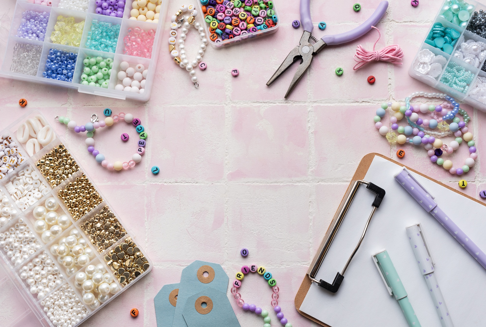 Colorful beads and jewelry making supplies arranged on pink tile background with clipboard and pens