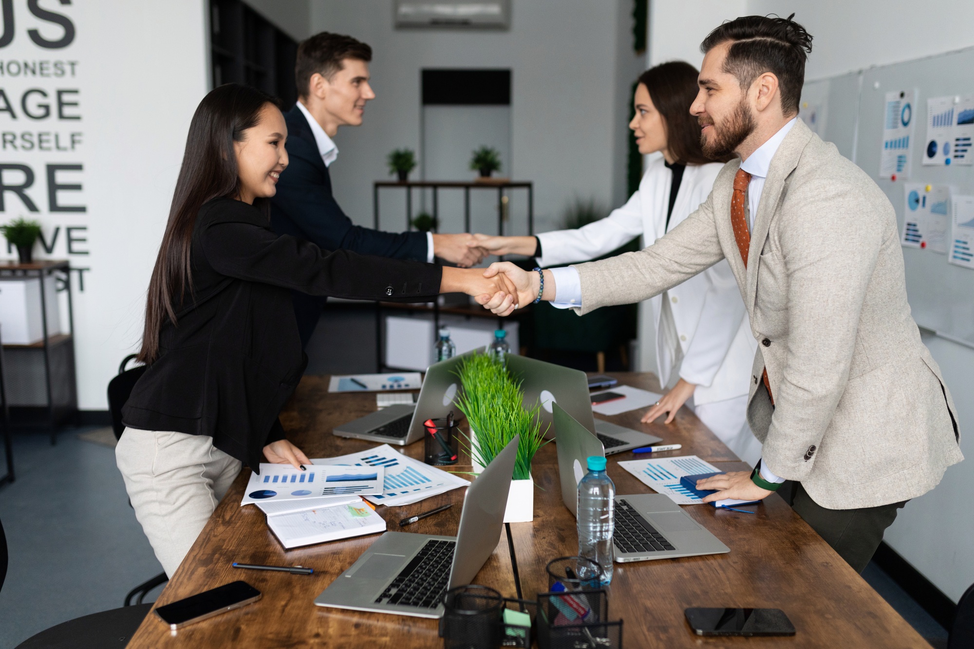 competitors company employees shake hands at a large table after successful negotiations