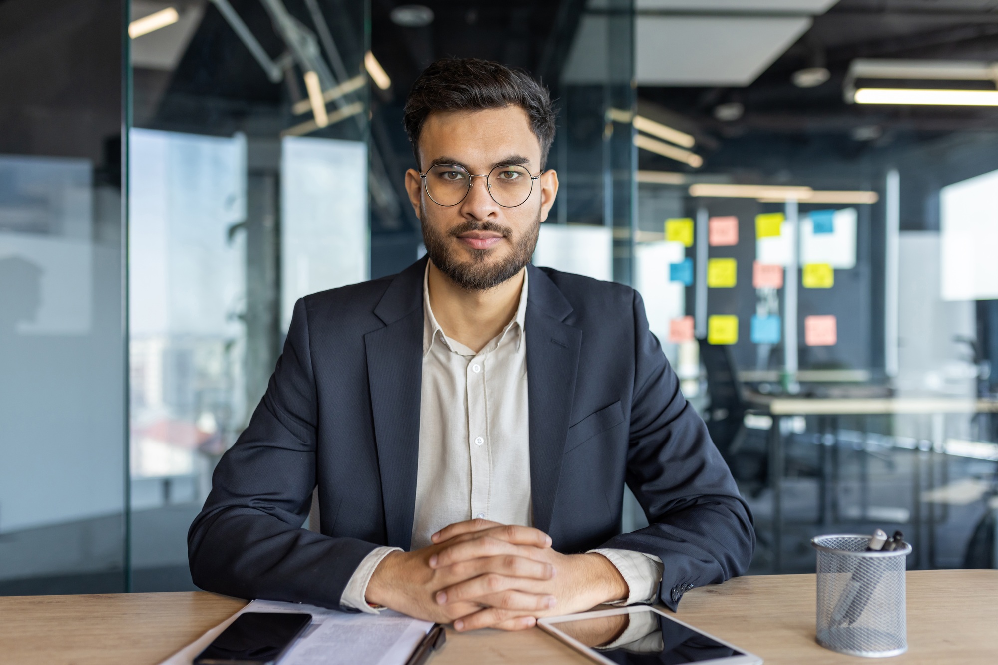 Confident businessman in a modern office with smart casual attire, seated at a desk with smartphone