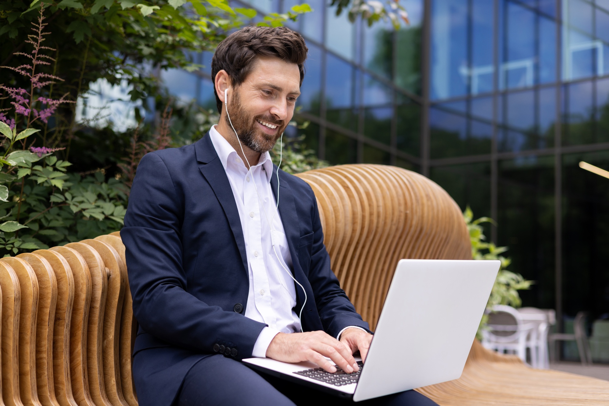 Confident businessman working on laptop at outdoor city park, professional with tech