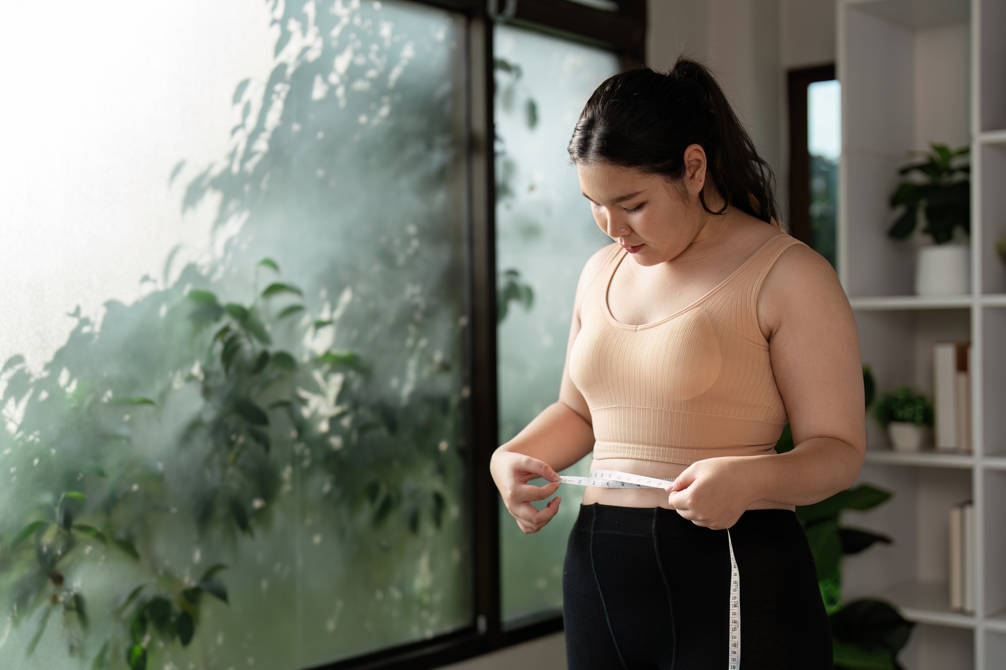Confident Woman Measuring Waist in Modern Home Gym Setting for Healthy Lifestyle and Fitness Goals