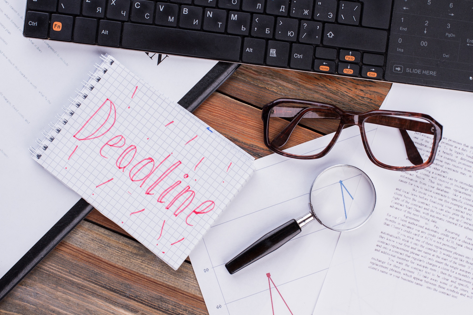 Deadline on notepad and various business papers on brown background.