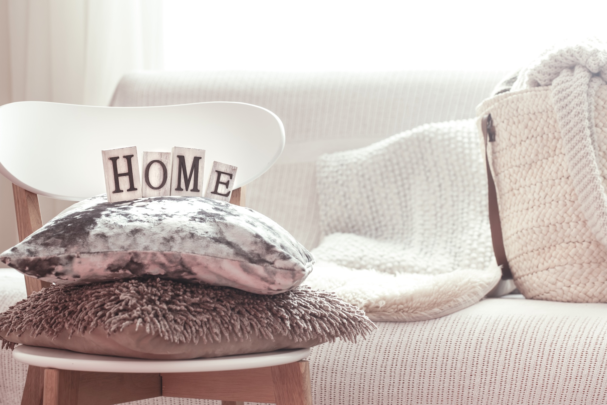 Decorative pillows and home lettering on white wooden stylish chair.