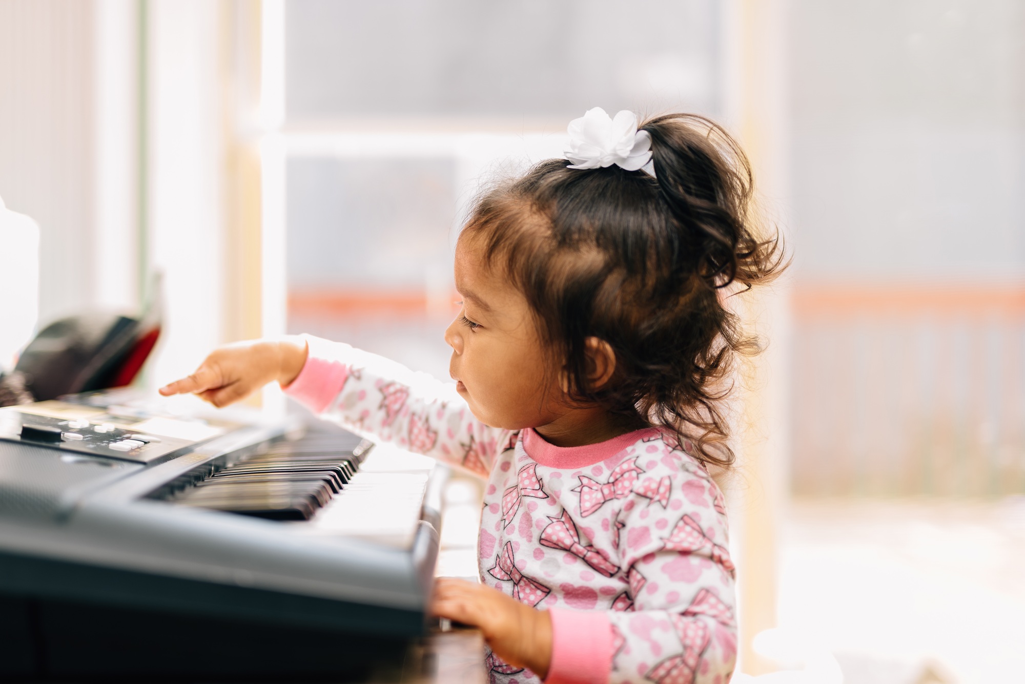 Diverse toddler girl at home playing on piano, learning, development