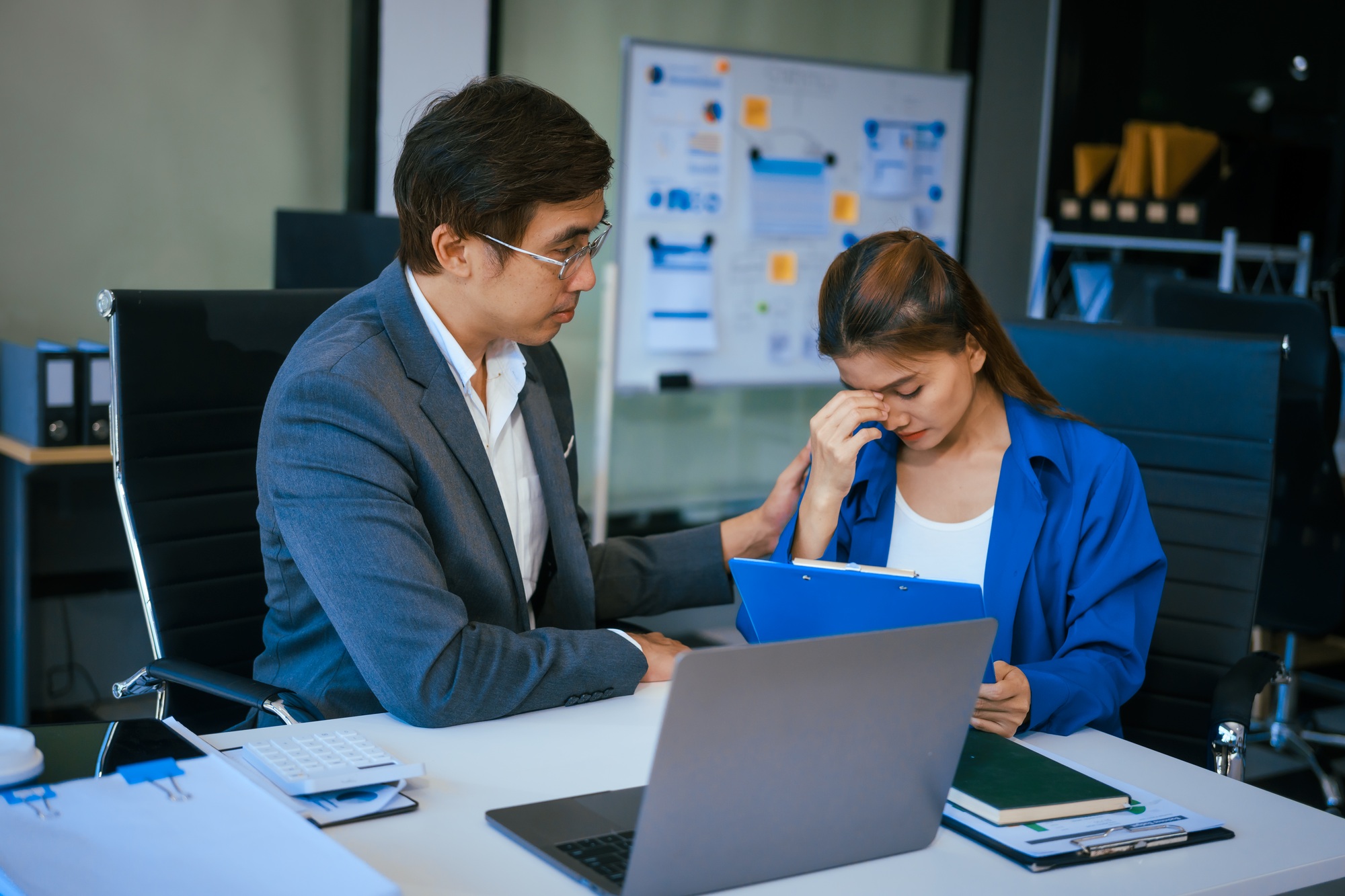 A stressed businessman and woman sit at a desk,overwhelmed by business challenges discuss problems