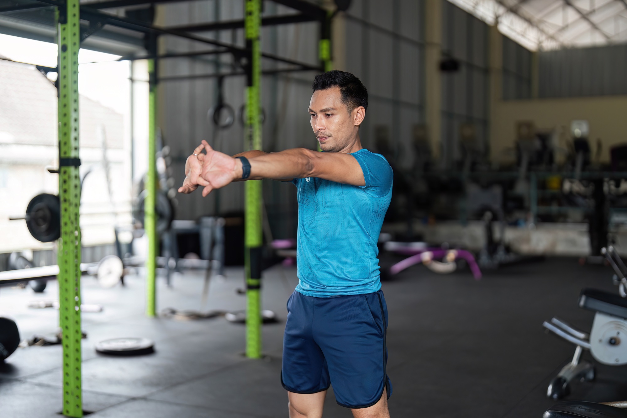 Fitness Training. Young man stretching arms in a gym setting.