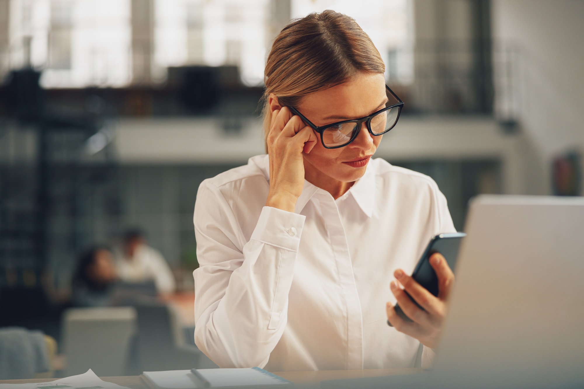 Focused woman sales manager use phone during working day in modern office