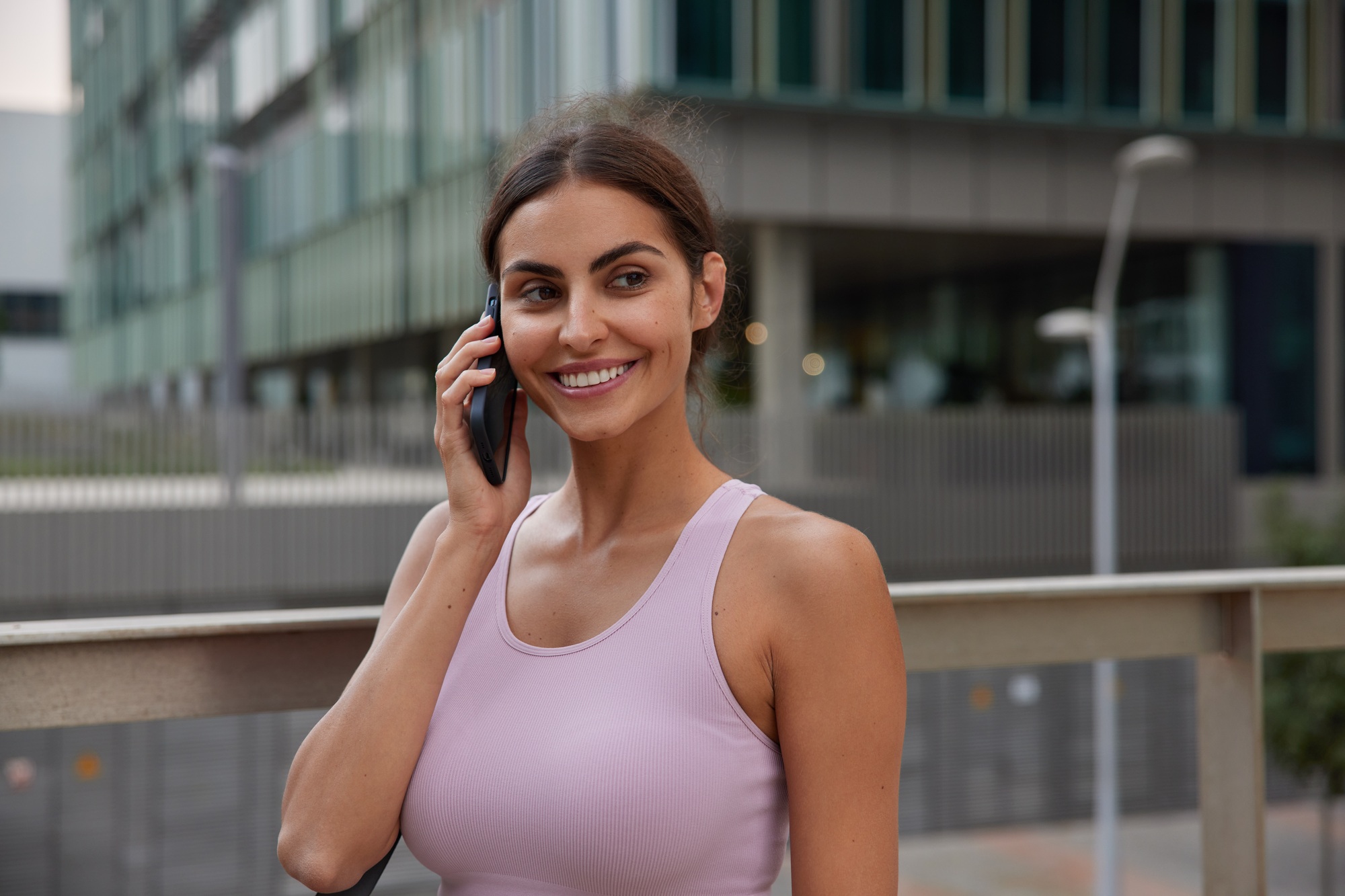 Good looking young sportswoman walks outdoors talks by phone enjoys communication time discusses fit