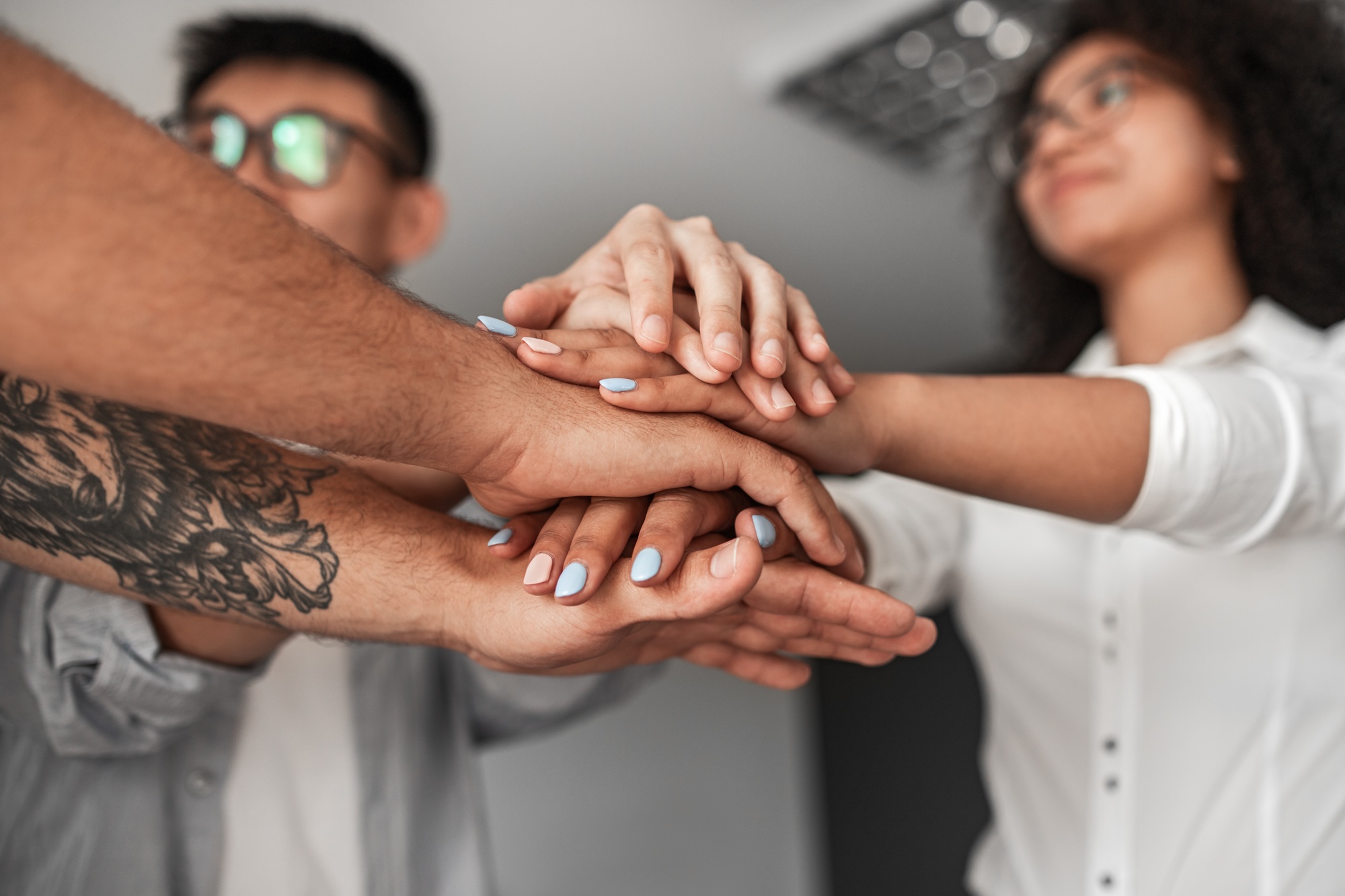 Group of positive multiracial colleagues stacking hands during team building