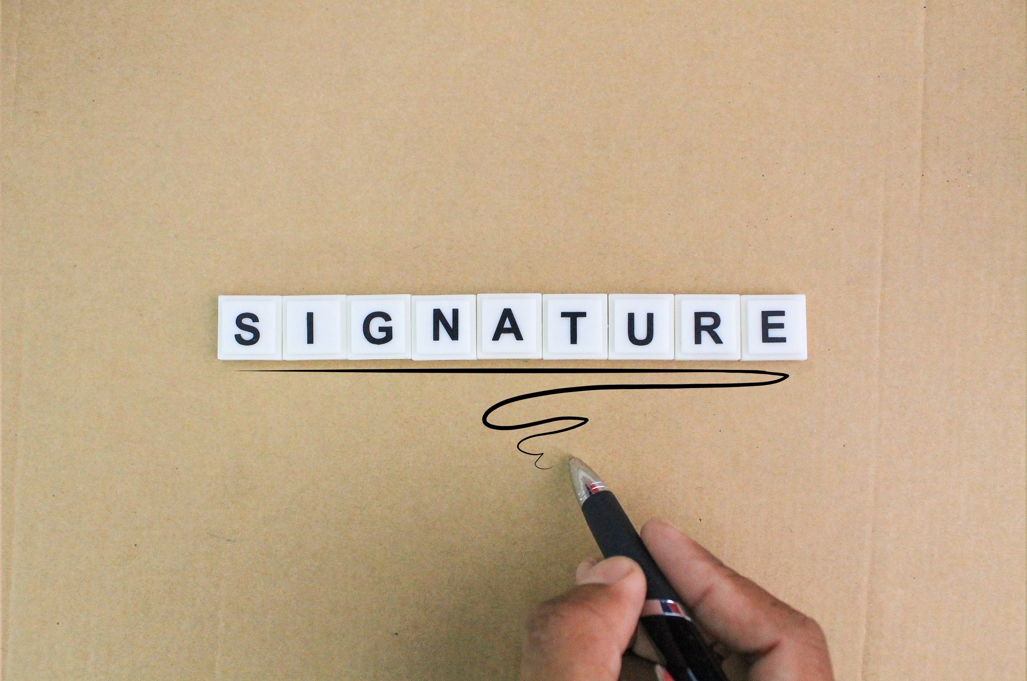 hand holding a pen and signing with the word Signature alphabet letters.