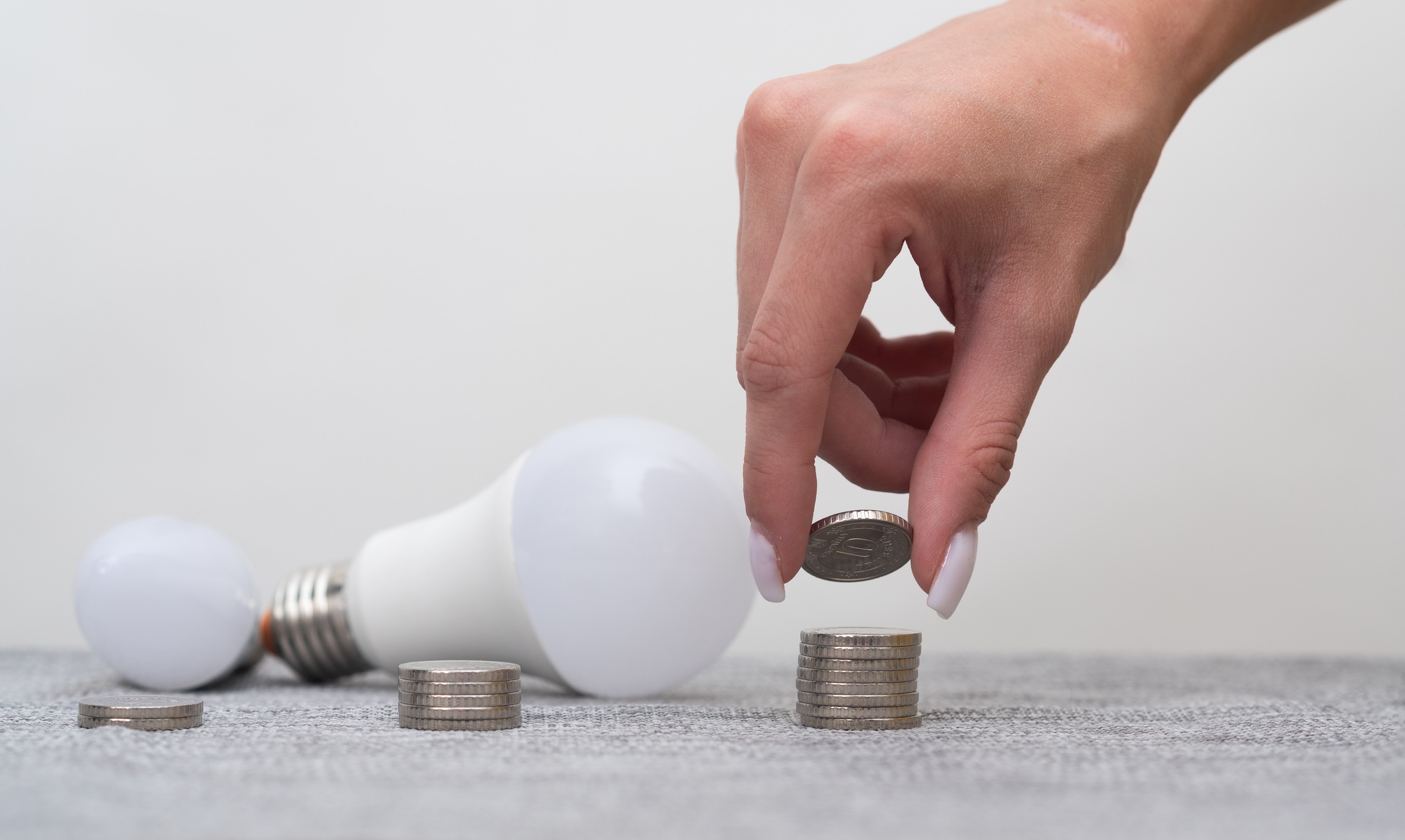 hand puts the coins in pile next to LED light bulb. concept cost saving and sustainability.