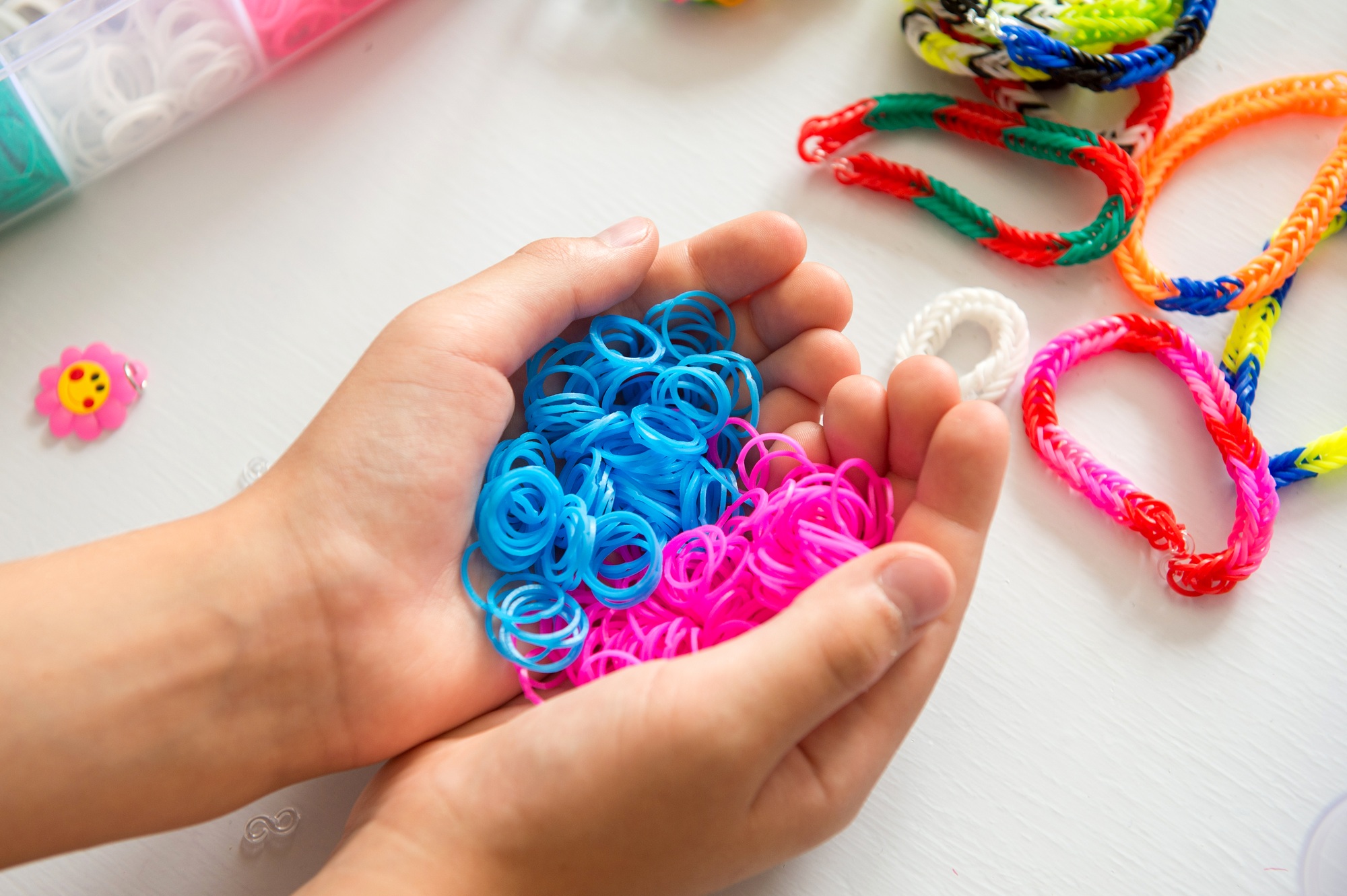 Hands holding blue and pink loom bands with other craft supplies in background.