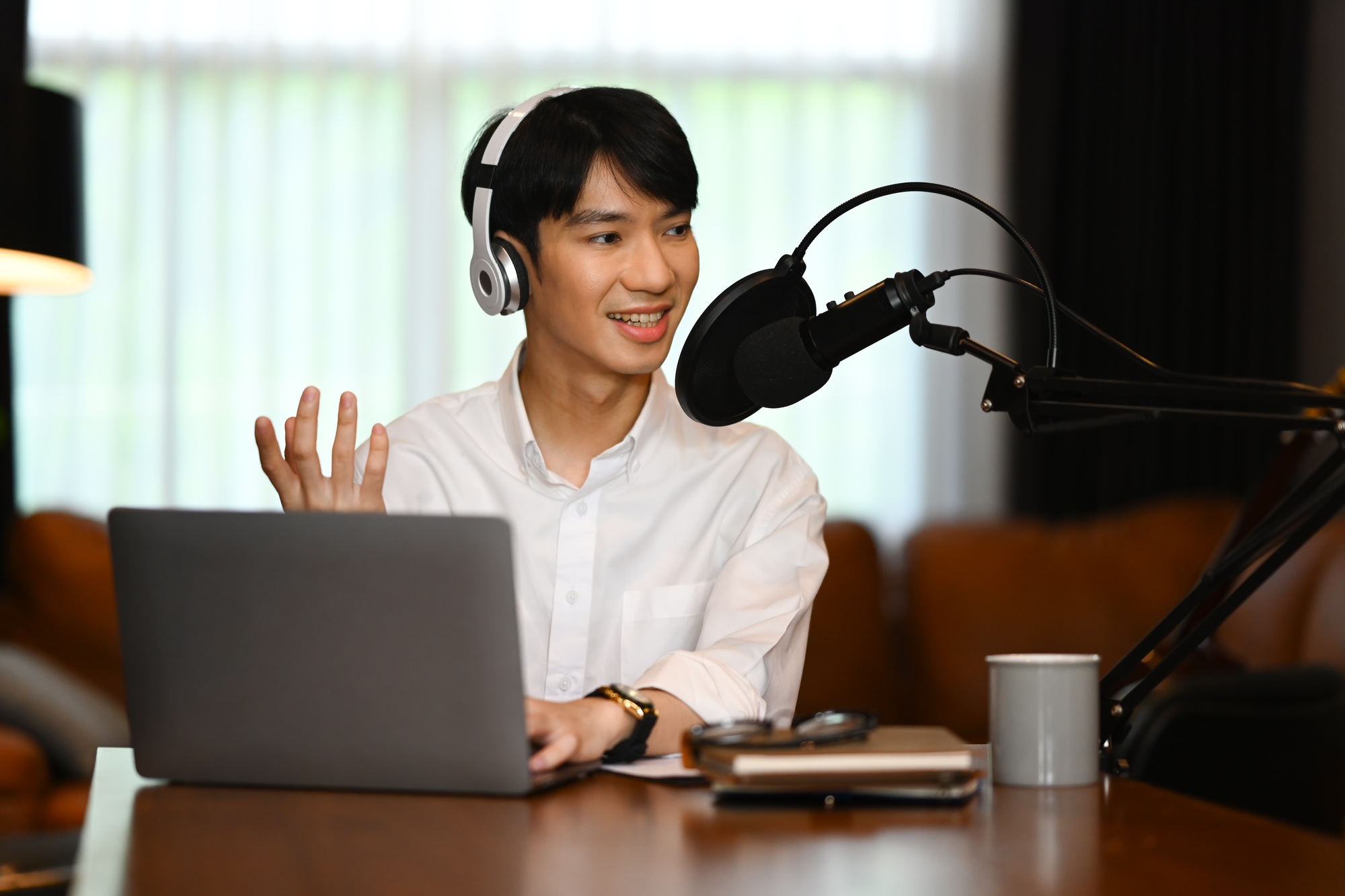 Handsome male radio host wearing headphone interviewing guest, recording podcast at home studio
