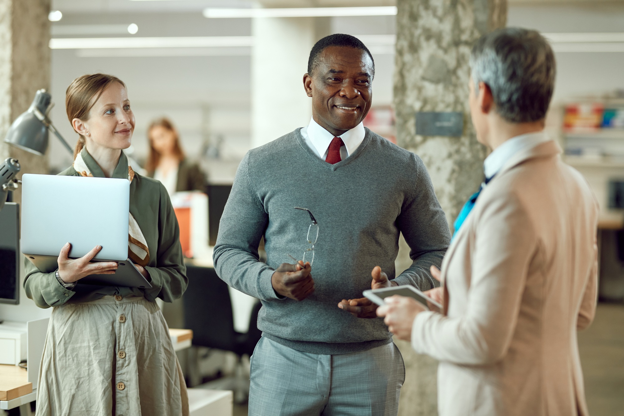 Happy African American executive communicating with female coworkers in the office.