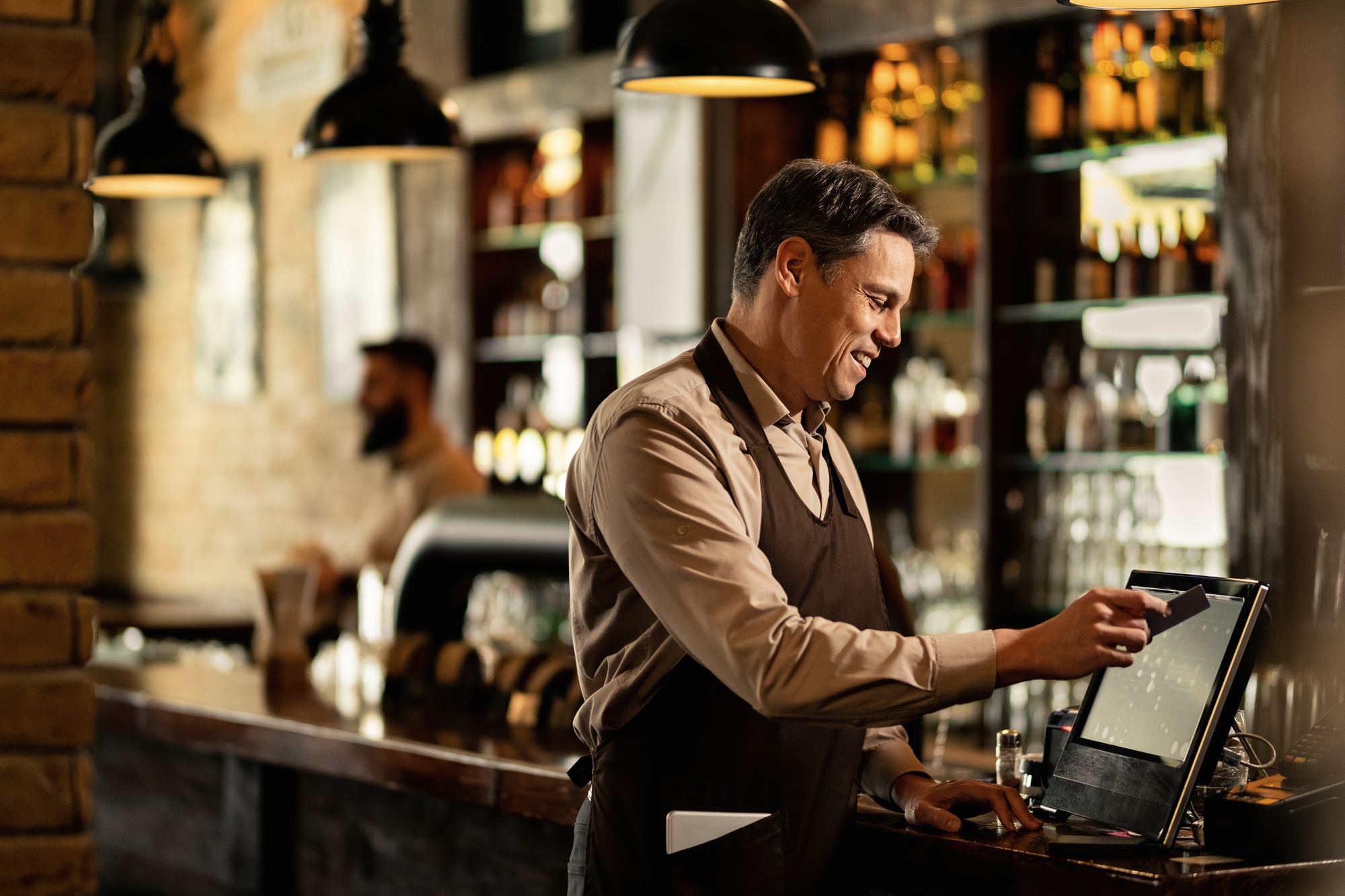 Happy barista working at point of sale in a bar.