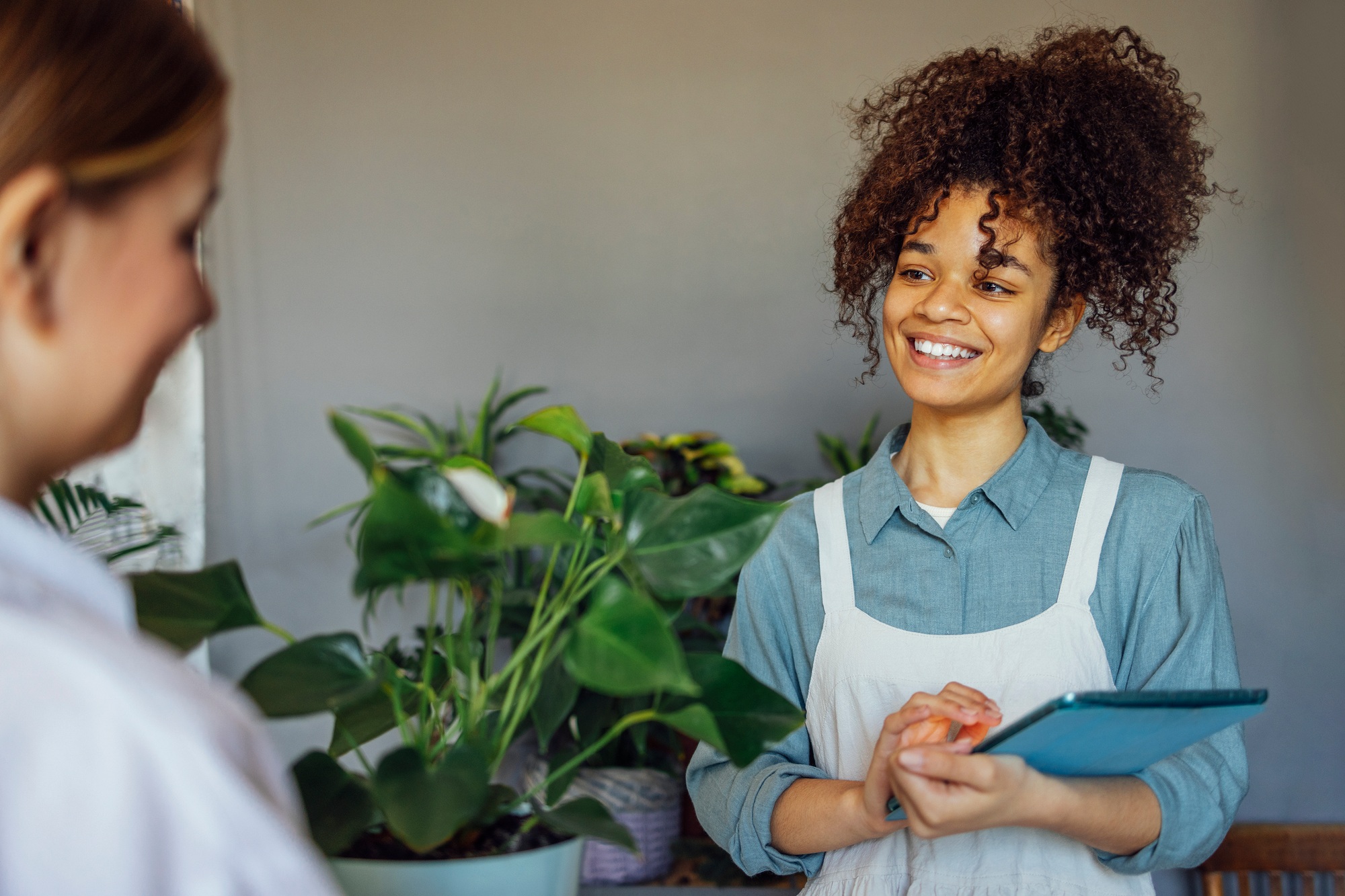 Happy black woman entrepreneur standing in plant store selling fresh flowers to client.