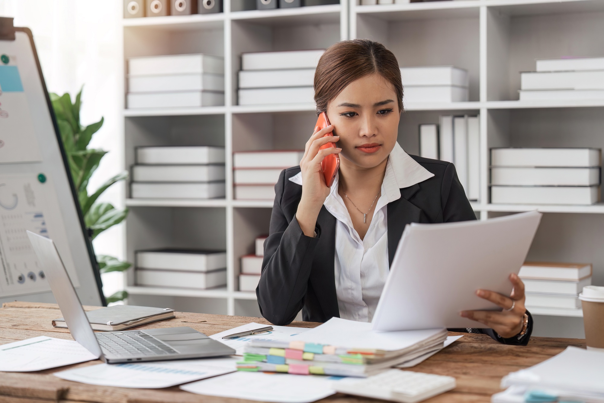 Happy businesswoman talking on mobile phone while analyzing weekly schedule in document