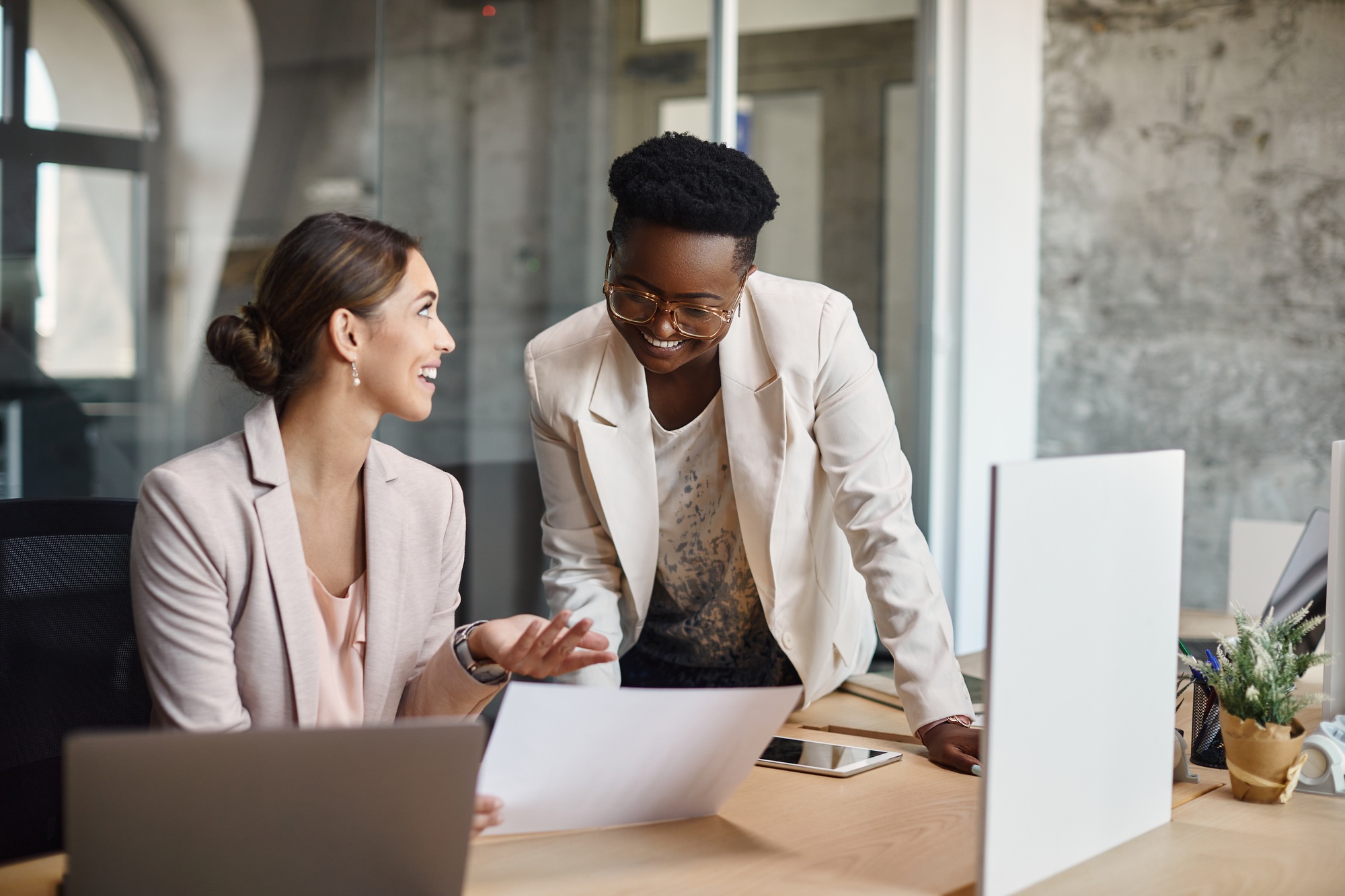 Happy businesswomen talking while analyzing plans and working in the office.