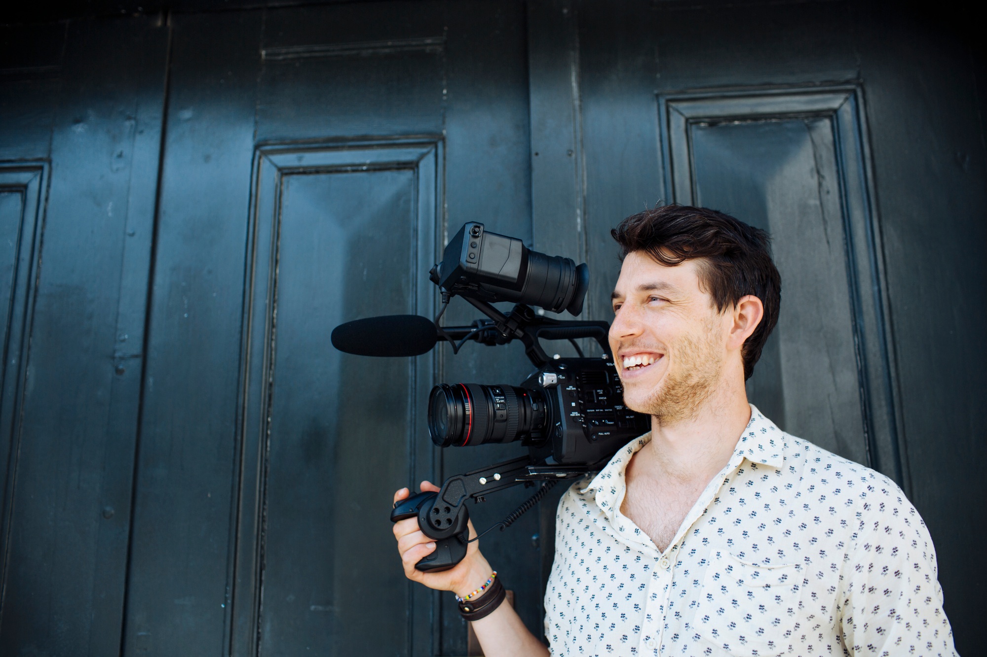 Happy man carrying digital video camera while standing against door