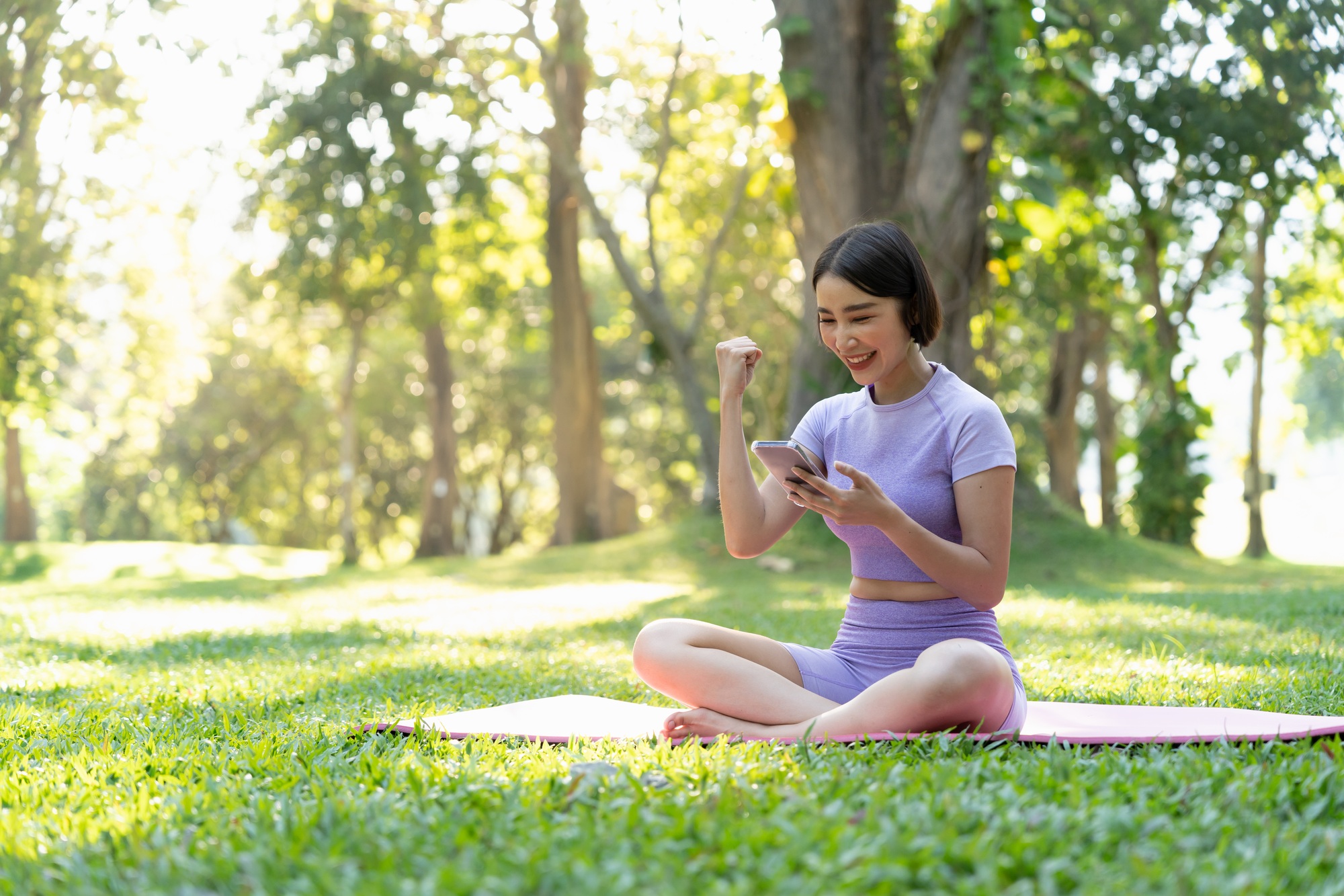 Happy sportswoman looking at her fitness app on mobile phone and triumphing, achieve daily goal in