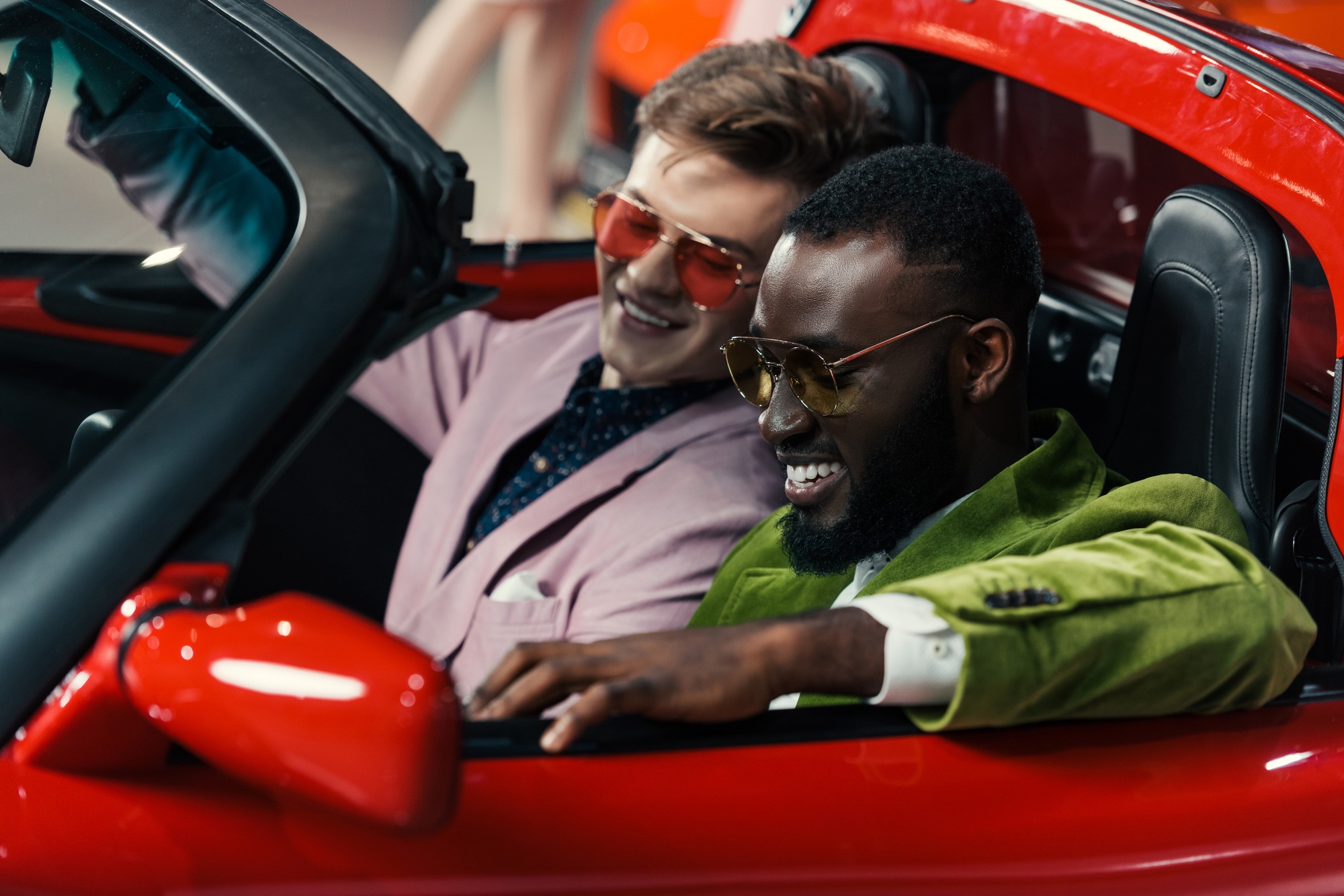 happy stylish multicultural men sitting in new car at showroom