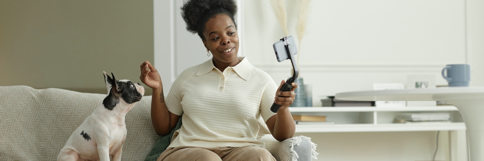 Header Image of Black Female Blogger Filming Video on Phone while Sitting on Couch with Dog at Home