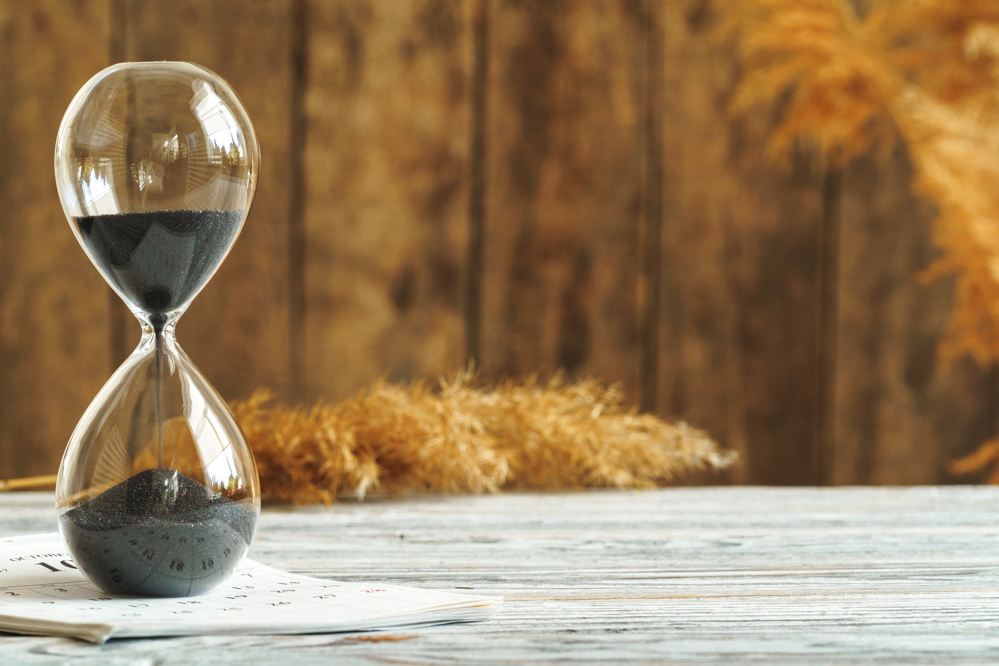 Hourglass with calendar on wooden desk close up