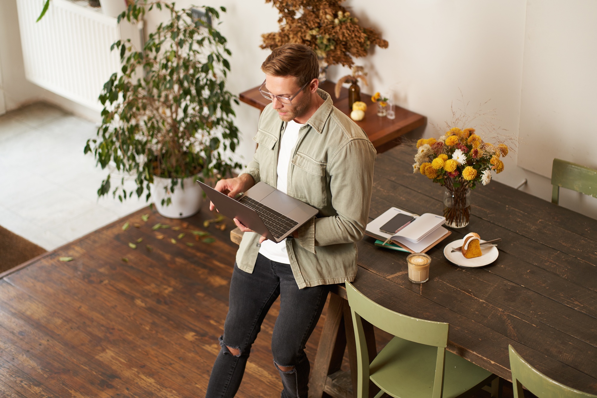 Image of young man, successful businessman sitting on table, looking at laptop, working in an