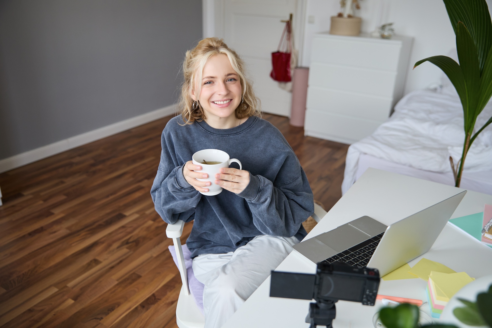 Image of young woman, social media influencer, editing her video on laptop, sits in a room with