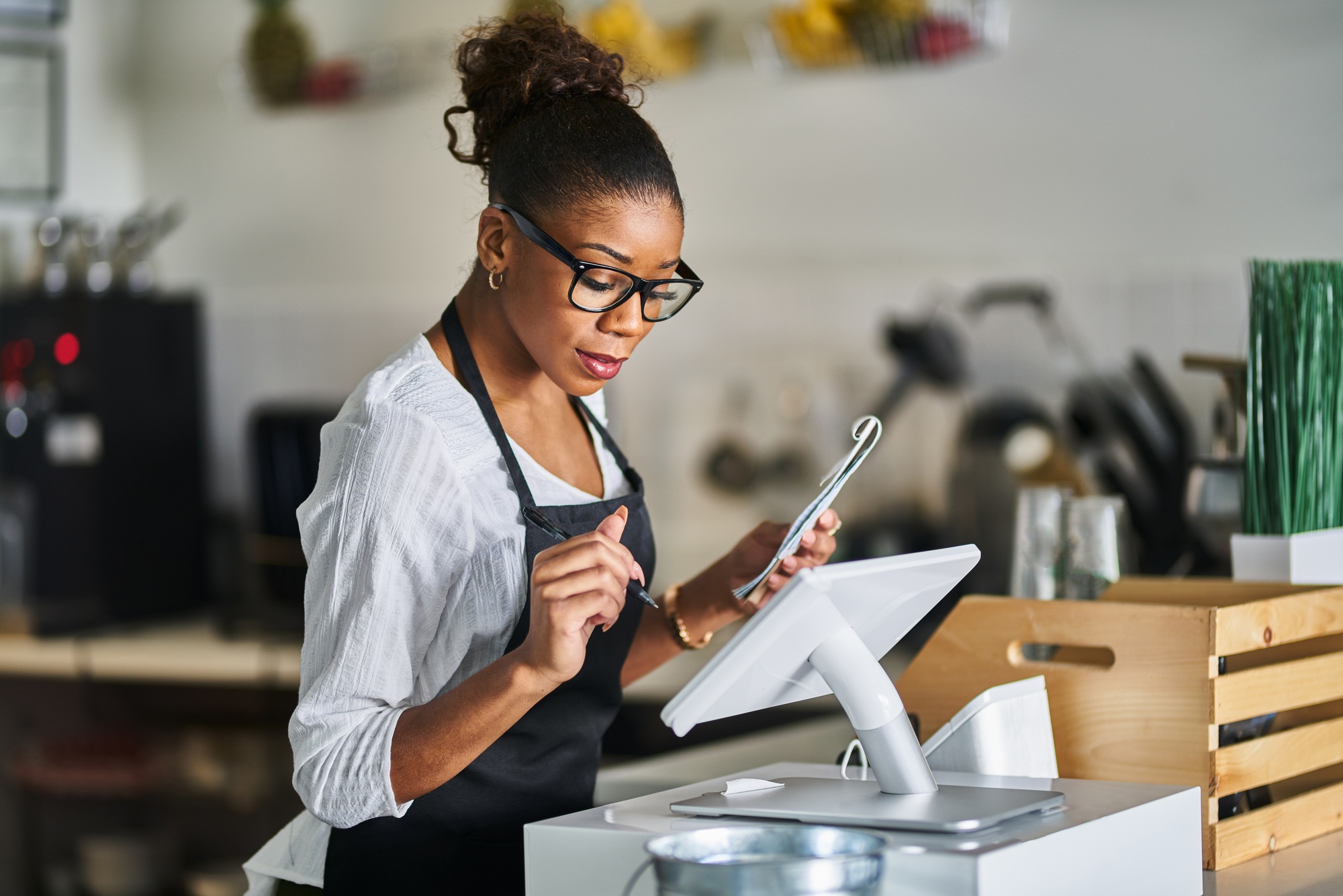 shop assistant placing order from notepad into pos point of sale terminal at register in restaurant