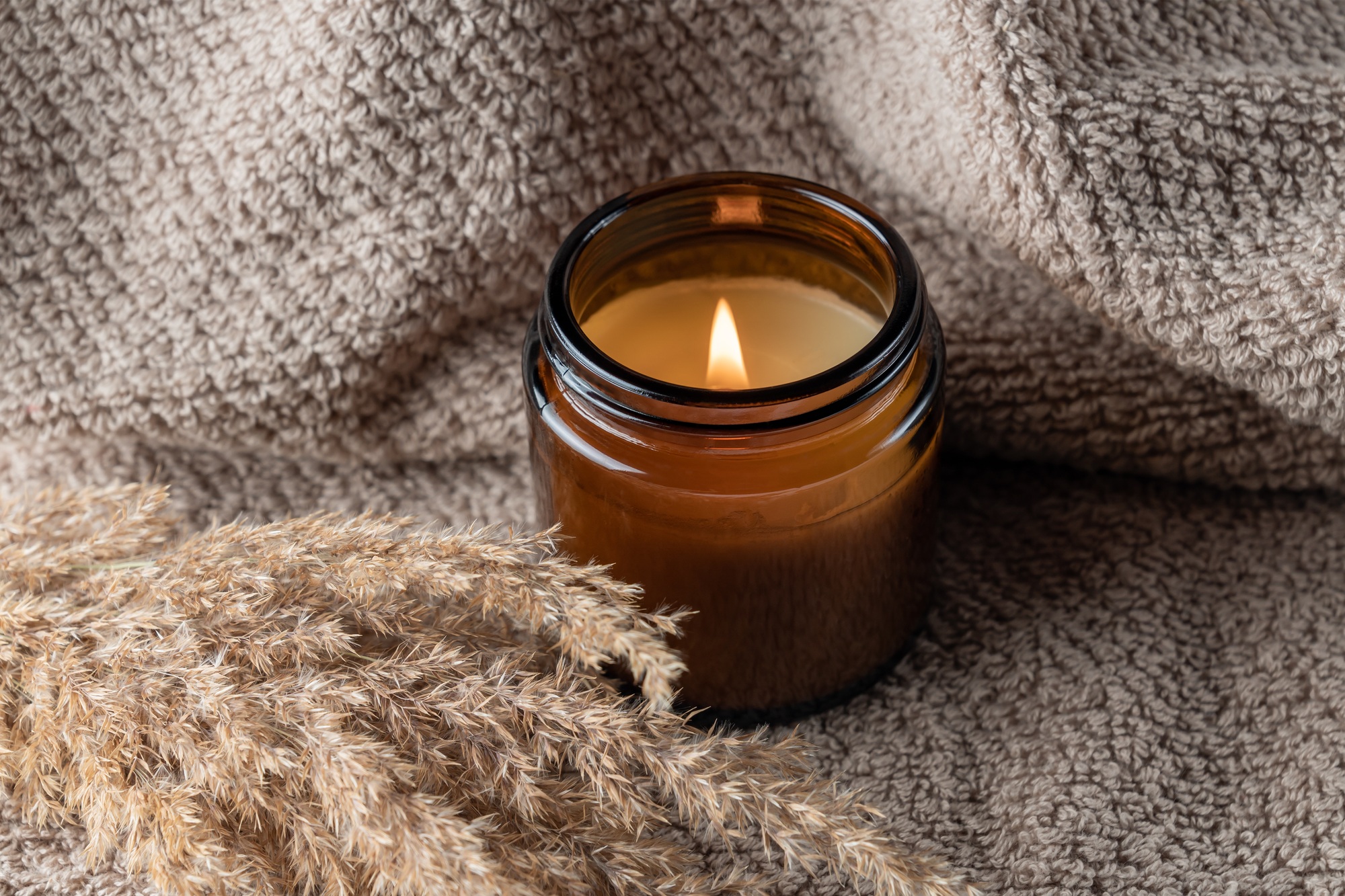 Label mockup of the glass jar with handmade candle on the coarse textile background with dry reed