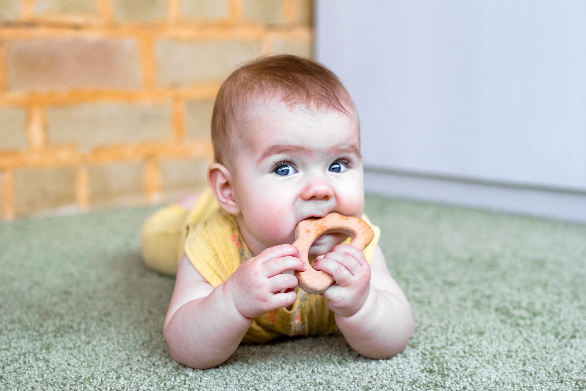 Little Caucasian baby girl with wooden teething toy. Eco-friendly toys for kids.