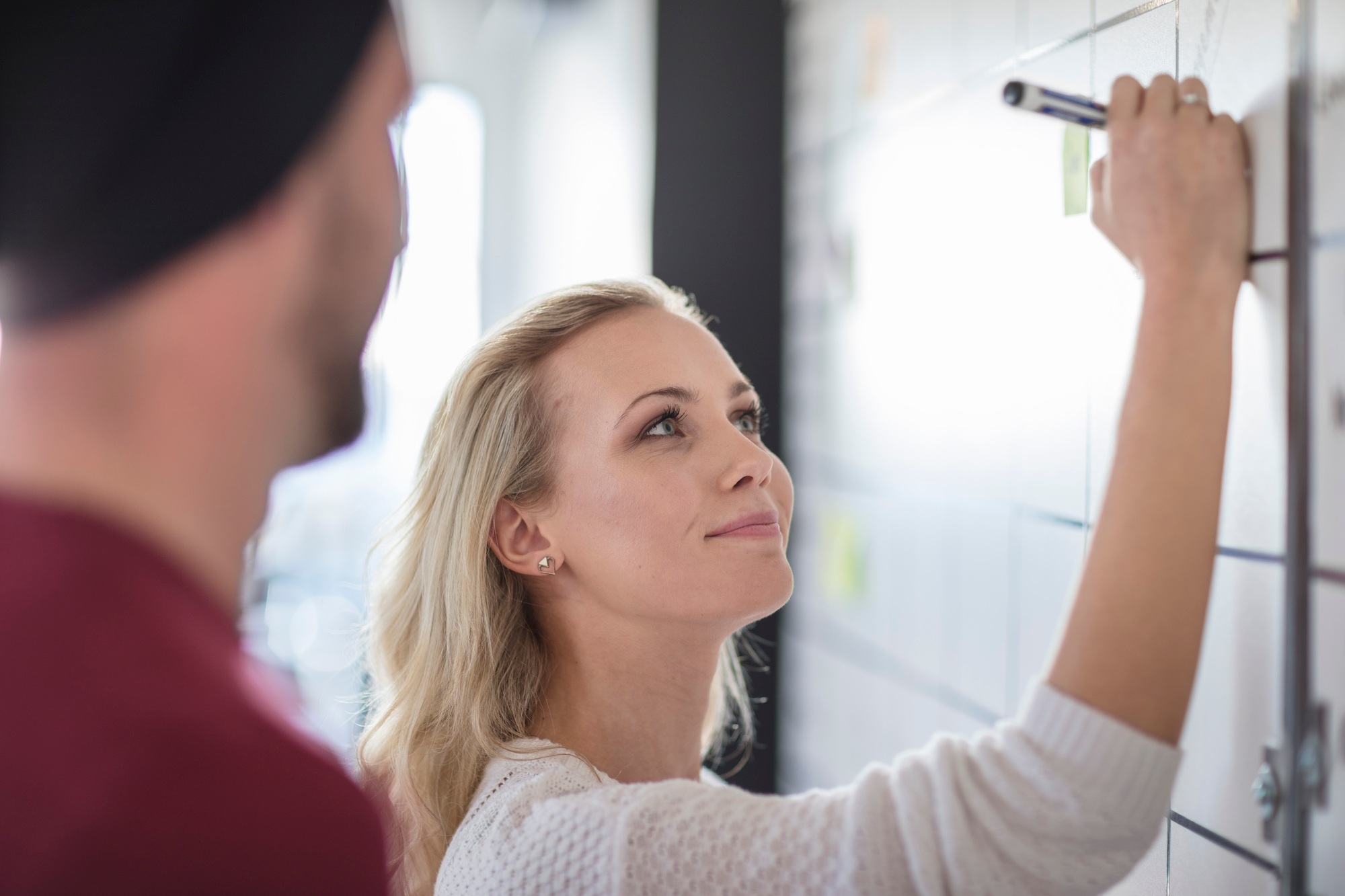 Male and female colleague planning ideas on office whiteboard, over shoulder view