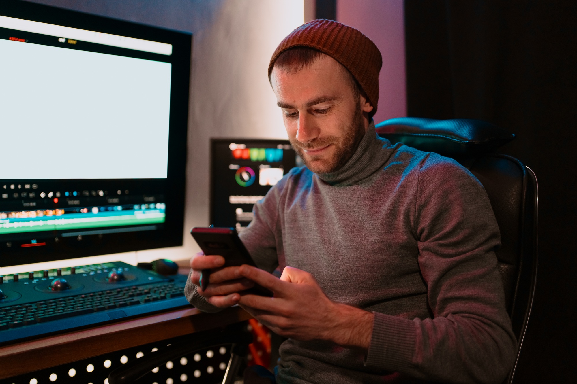 Male Video Editor sitting at his Computer using phone