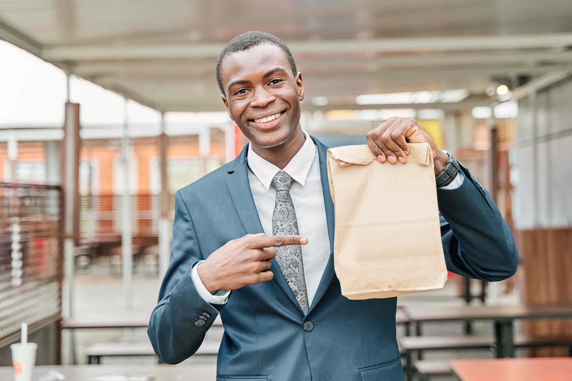 man in suit and tie points to paper bag with copy space for text or logo