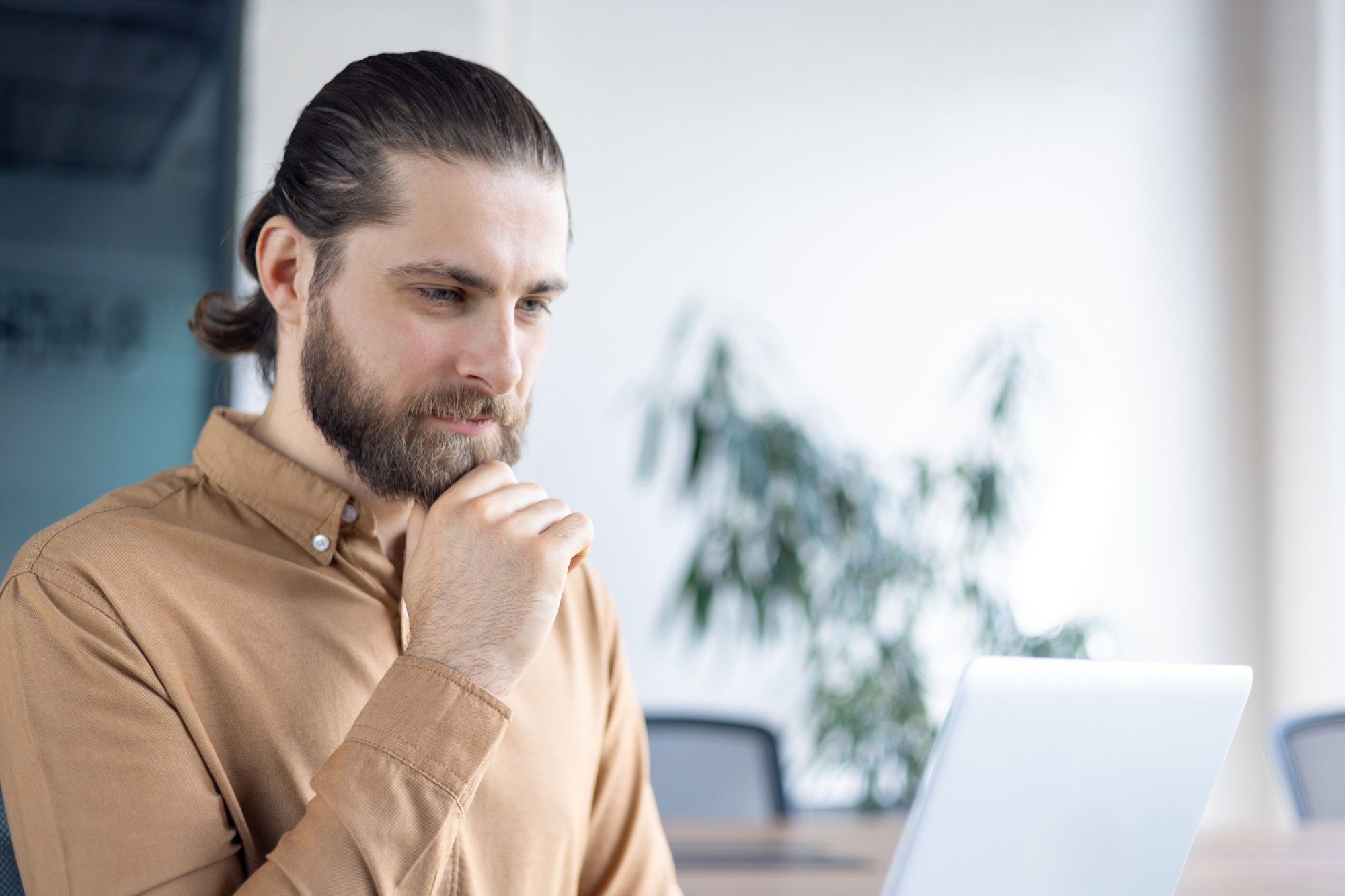 Man thoughtfully working on his laptop in a bright modern office