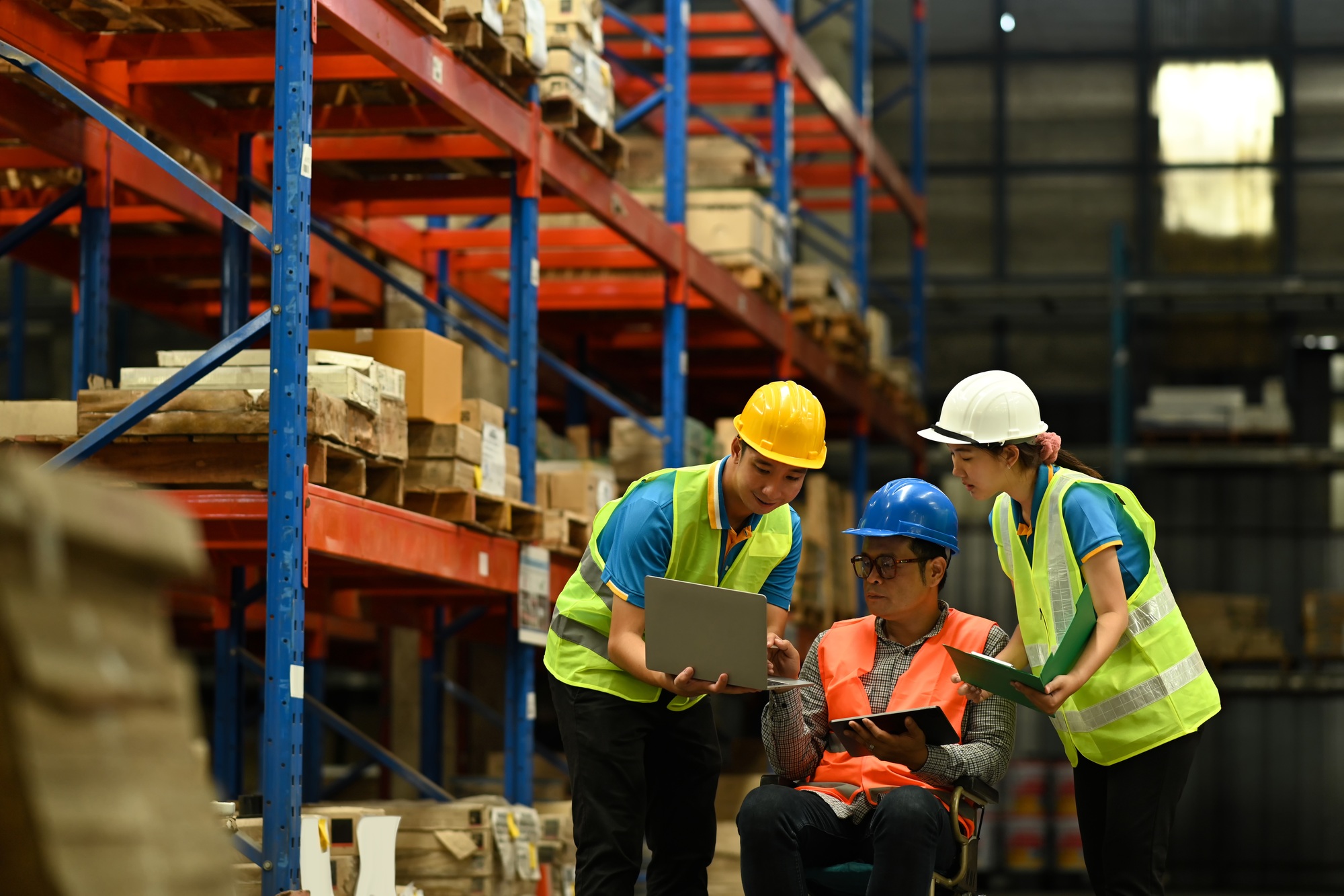 Manager and young workers using laptop with inventory checking software in retail warehouse.