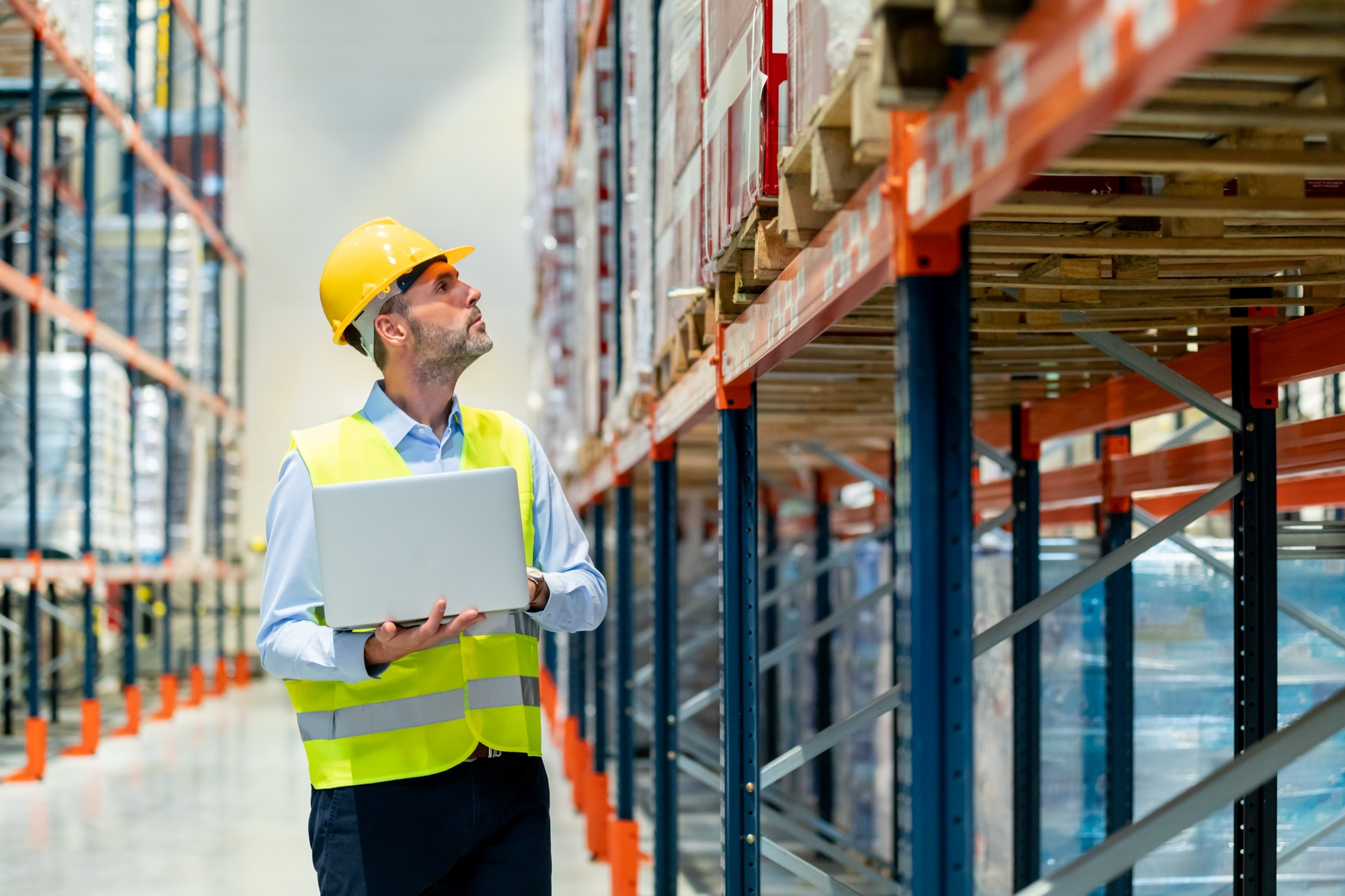 Manager of warehouse check inventory with laptop walking between shelves