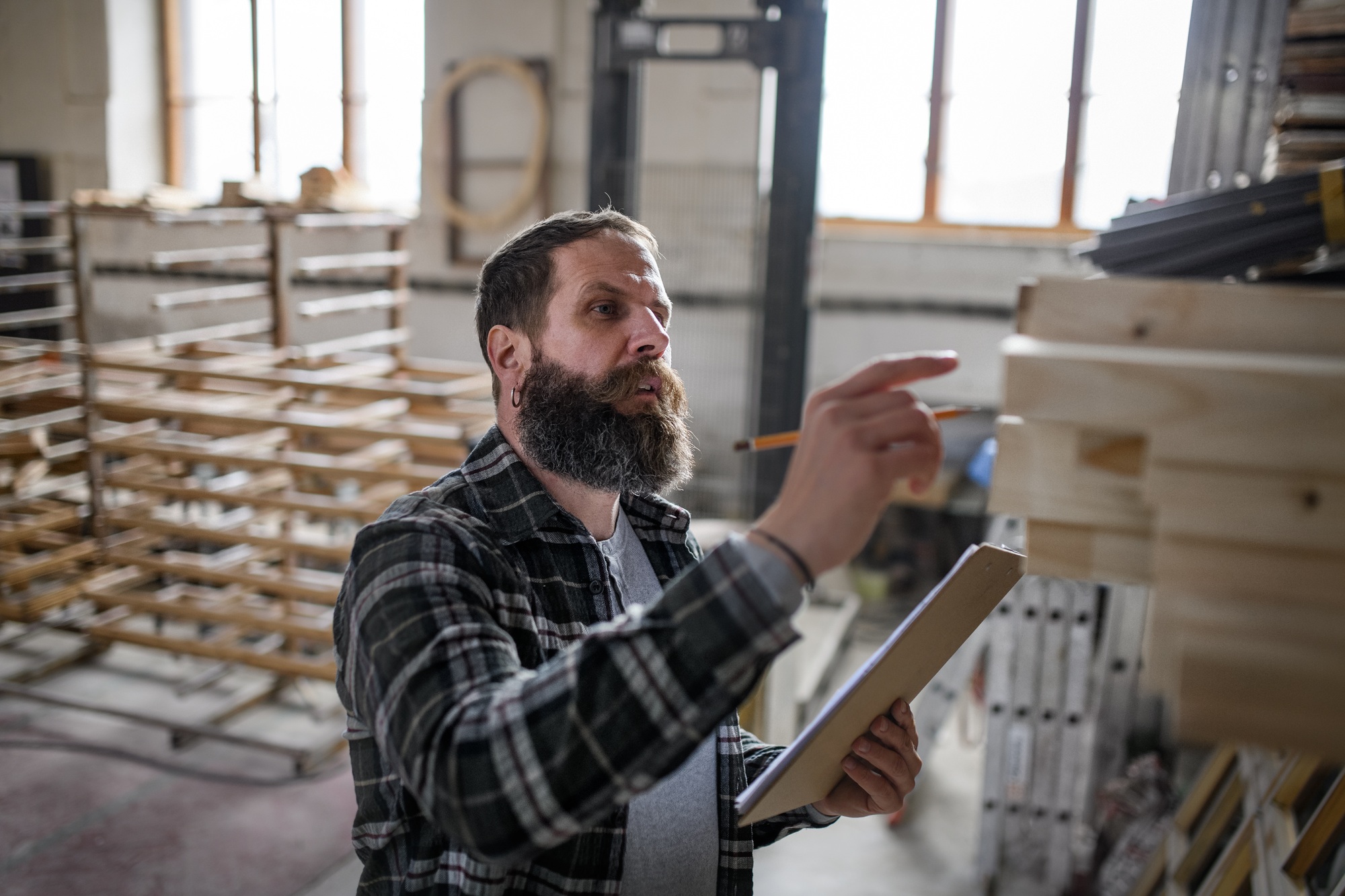 Mature male carpenter checking inventory indoors in carpentery workshop. Small business concept