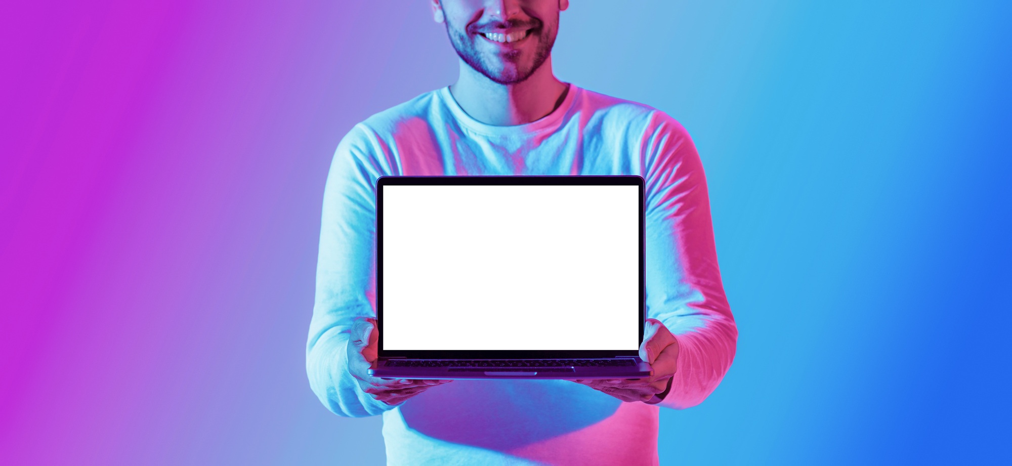 Millennial smiling guy shows laptop with blank luminous screen, cropped