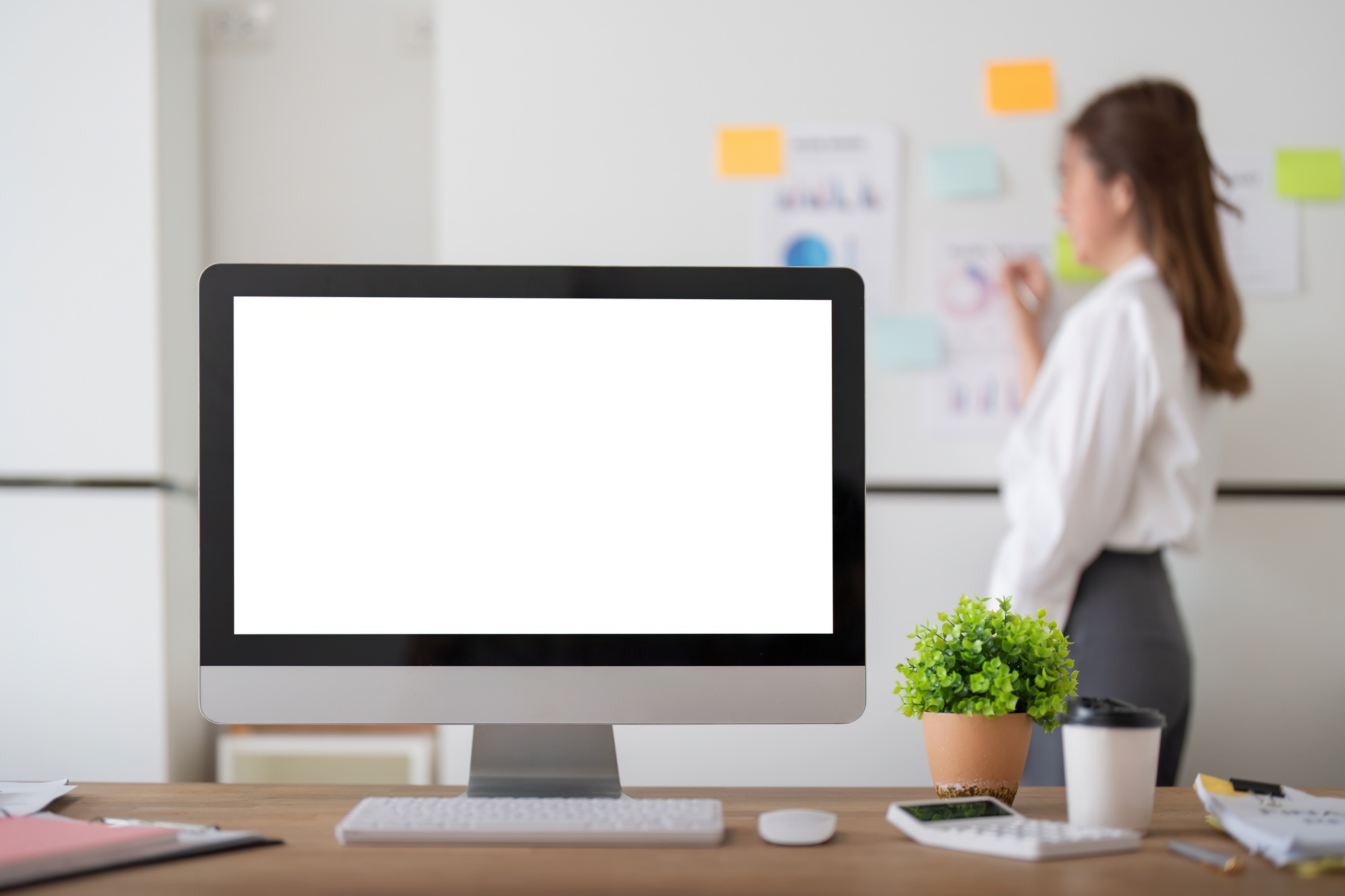 Mock up computer on wooden table with businesswoman analysis graph on a whiteboard in background