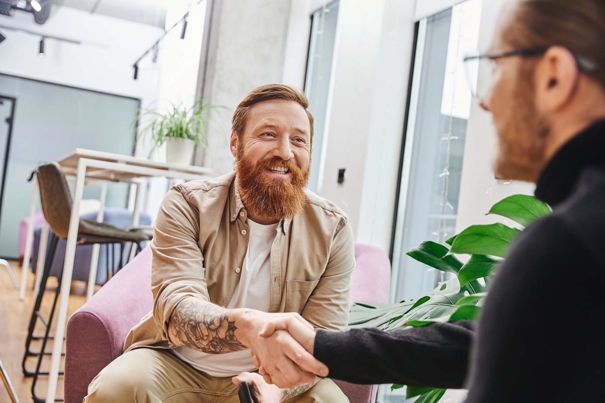 overjoyed, tattooed and bearded entrepreneur in casual clothes confirming agreement and shaking
