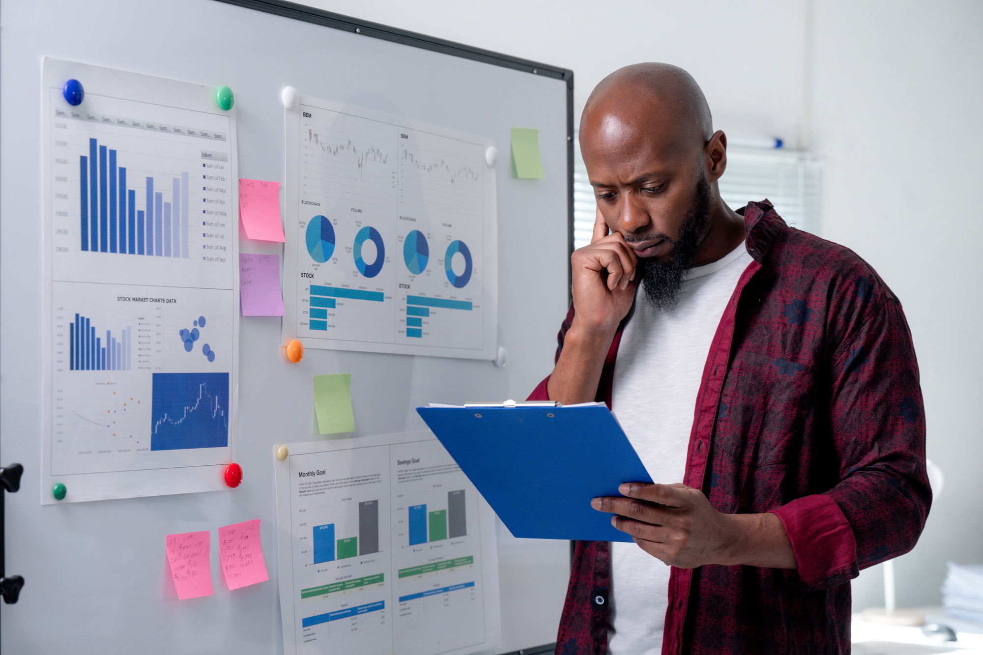 Pensive businessman analyzing data on clipboard, evaluating performance and strategizing for success in a modern office environment