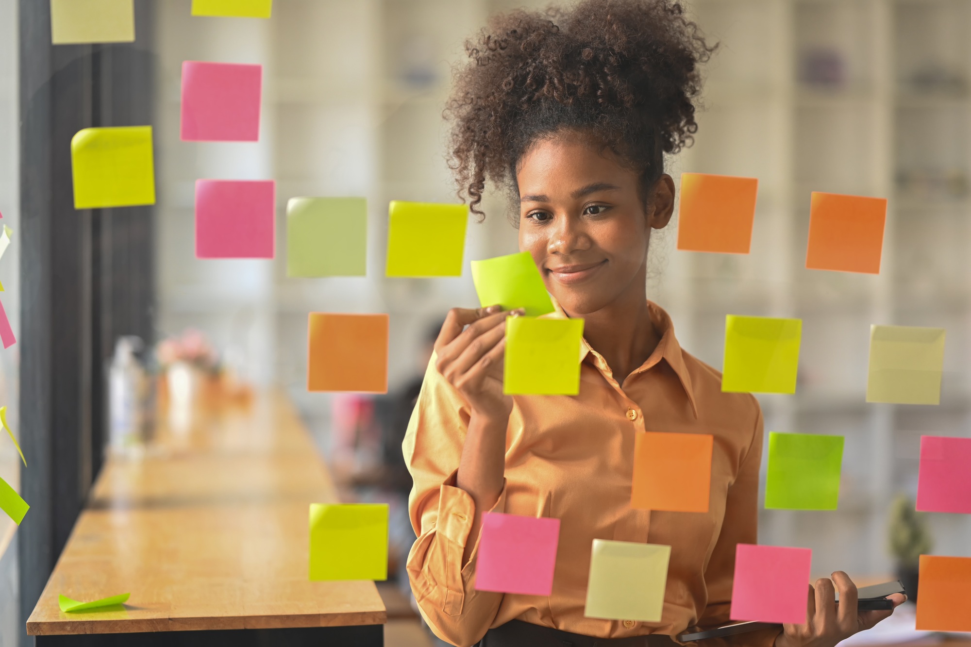 Pleasant African American business woman analyzing schedule, looking at sticky notes on board.
