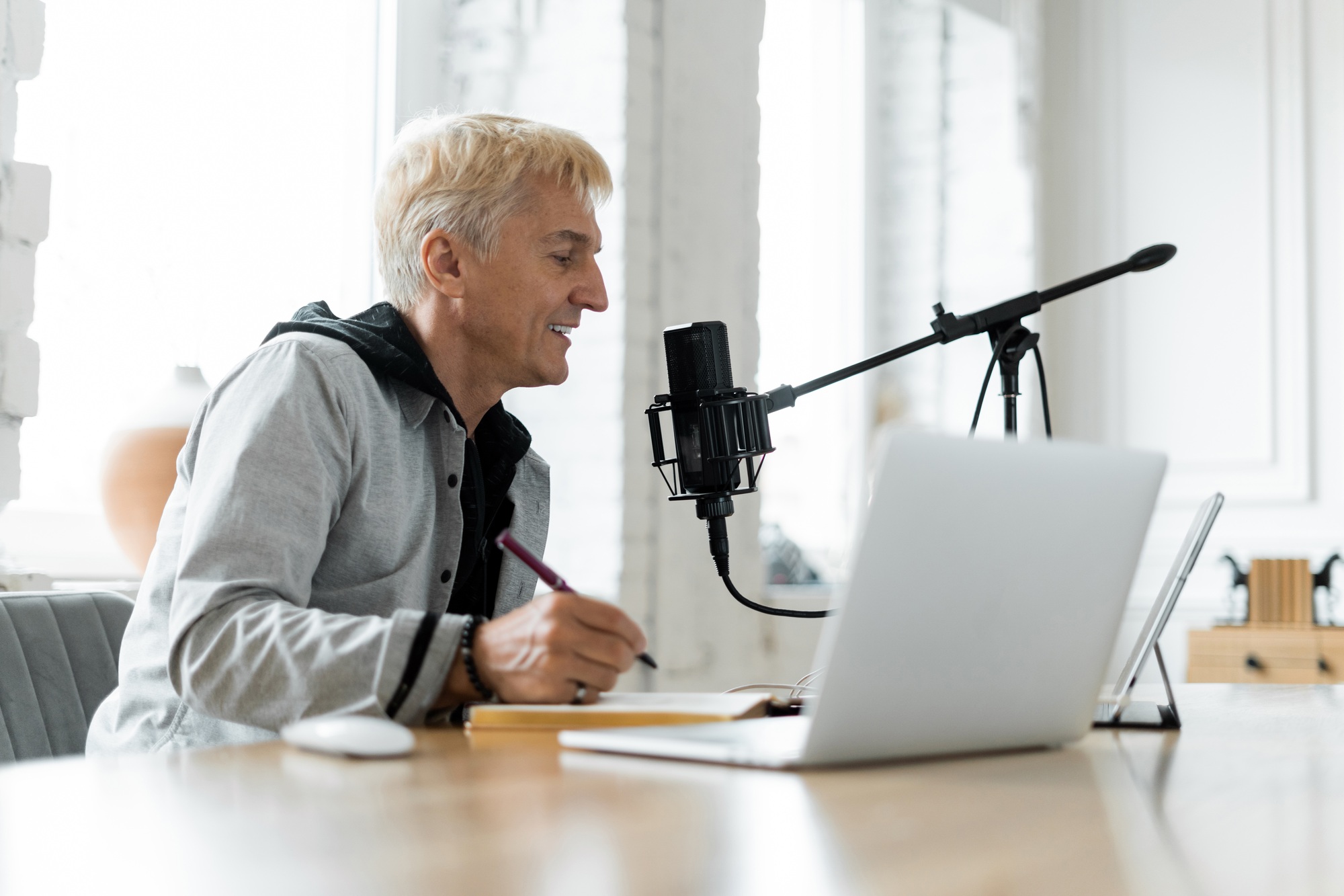 Podcaster recording a new episode, smiling as he speaks into a professional microphone, with laptop