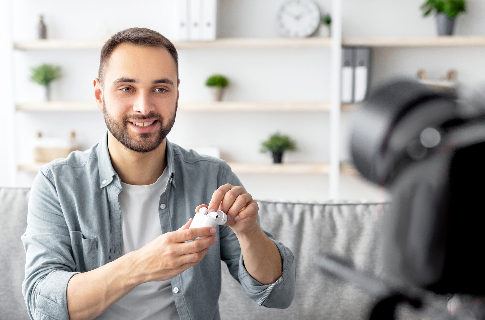 Popular male blogger shooting video review of new earhpones, using professional camera at home